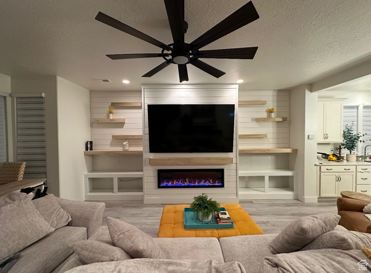 Living room featuring a fireplace, ceiling fan, light wood-type flooring, and a textured ceiling