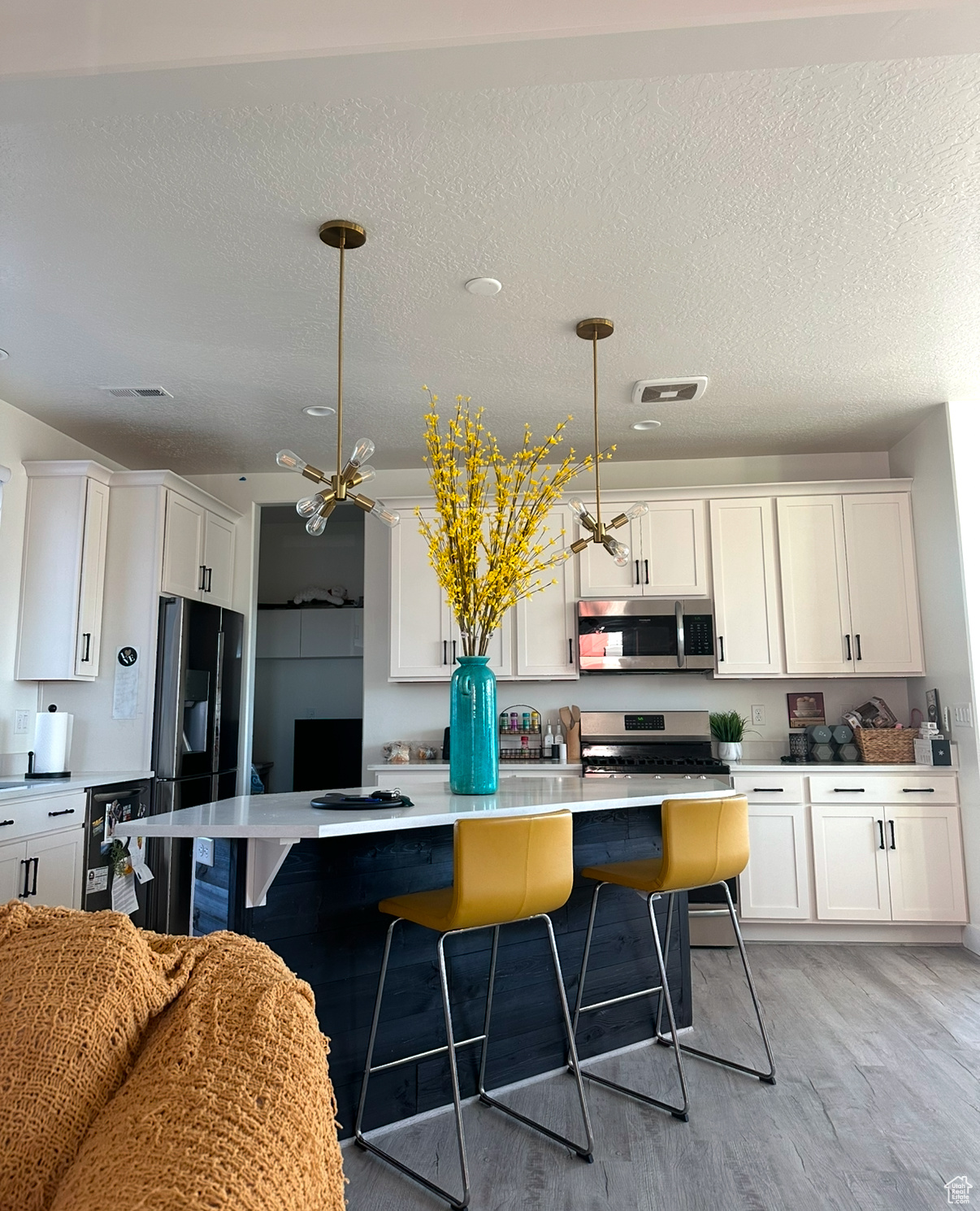 Kitchen featuring hanging light fixtures, light hardwood / wood-style floors, a breakfast bar, white cabinets, and appliances with stainless steel finishes