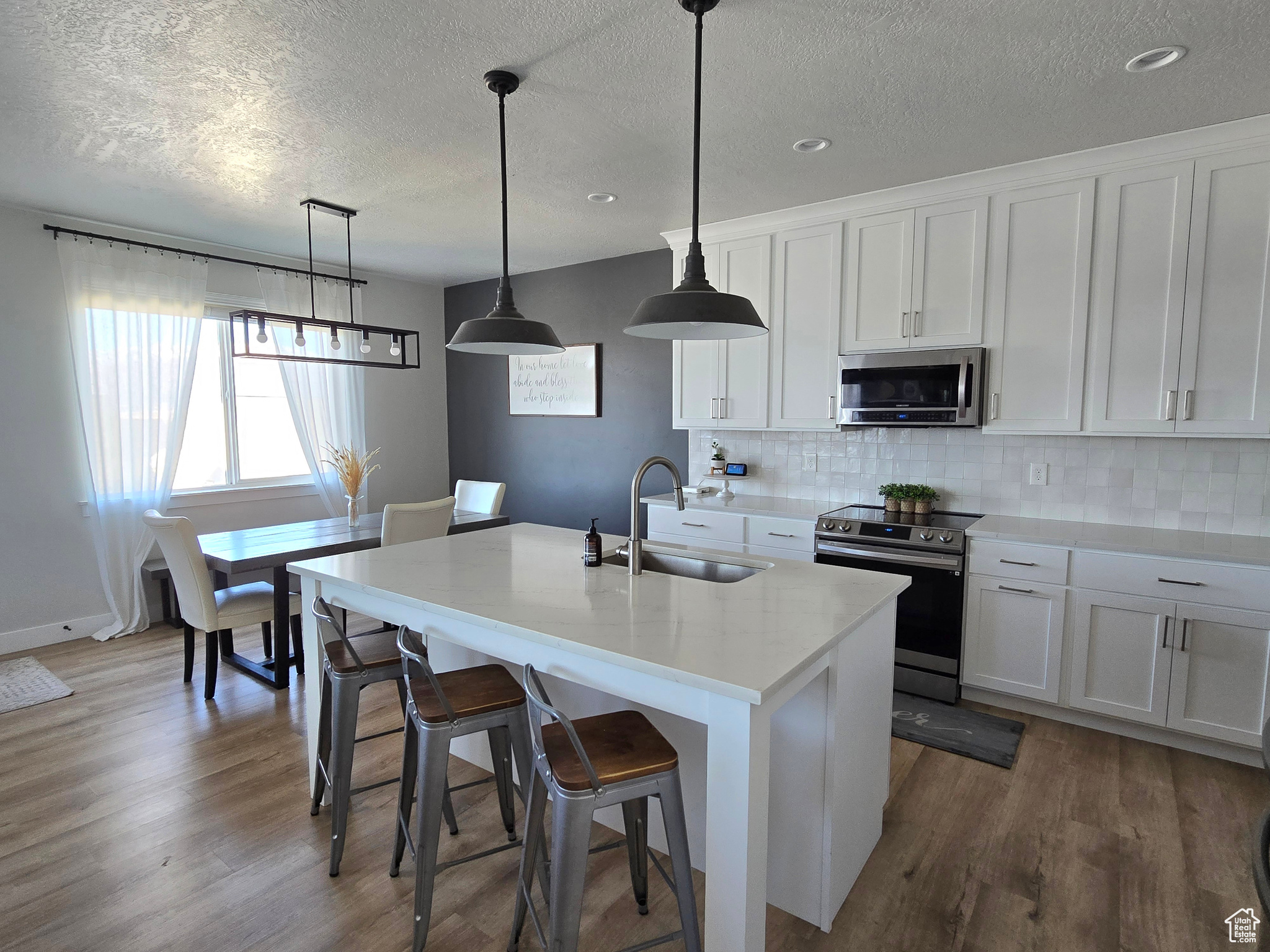 Kitchen with stainless steel appliances, a kitchen island with sink, sink, pendant lighting, and white cabinets