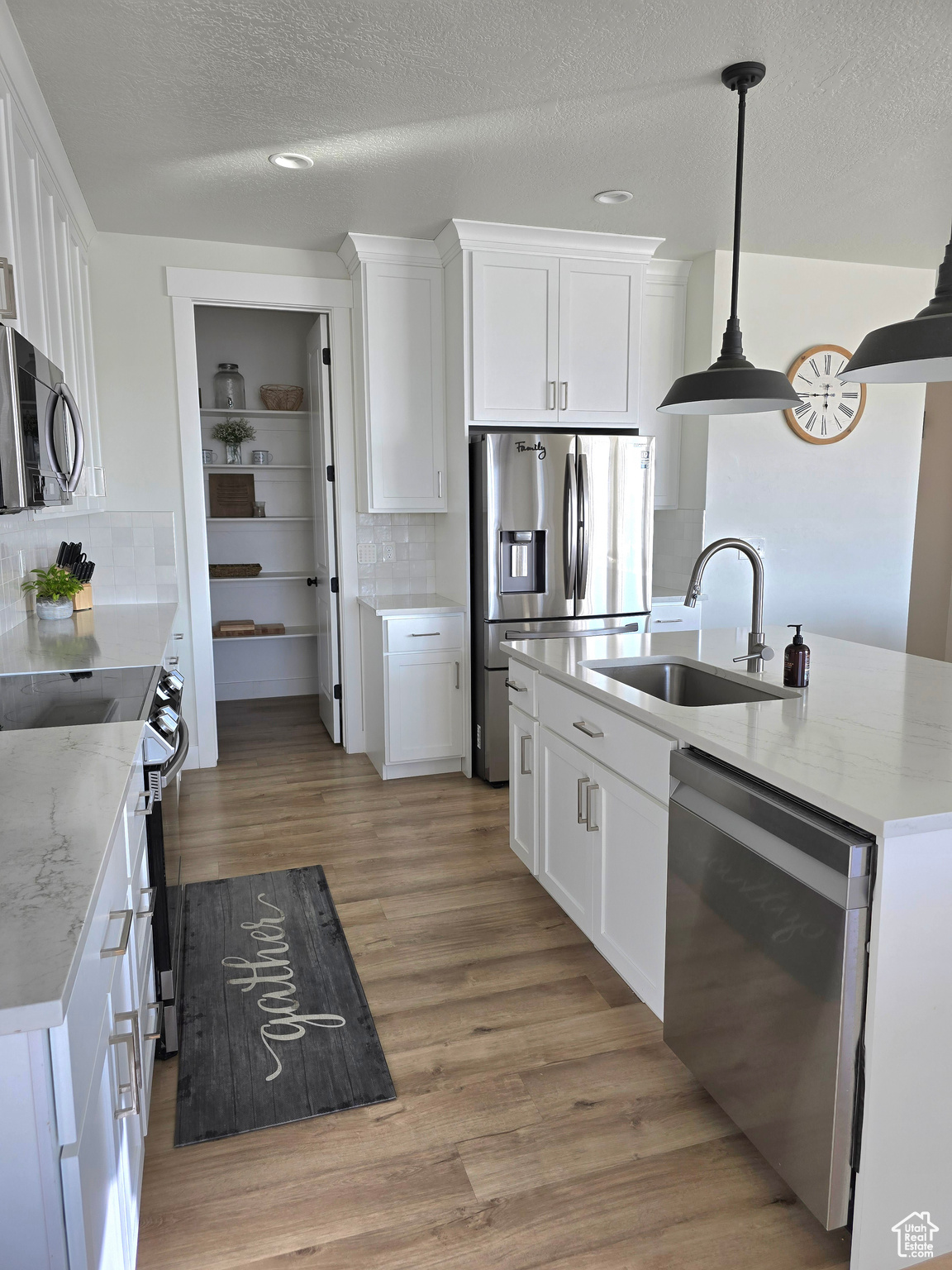 Kitchen with appliances with stainless steel finishes, light wood-type flooring, sink, pendant lighting, and white cabinetry