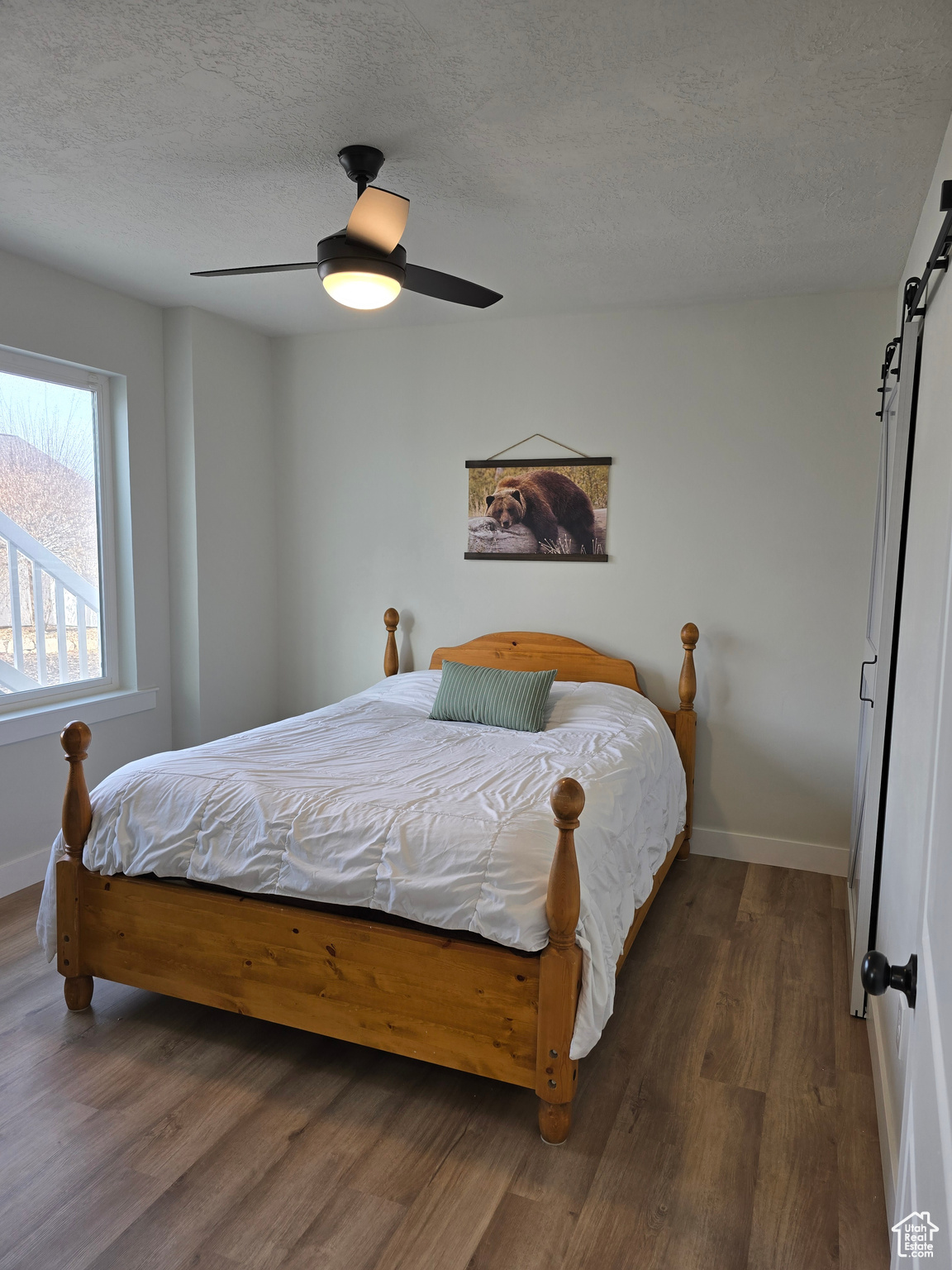 Bedroom featuring a textured ceiling, a barn door, ceiling fan, and wood-type flooring