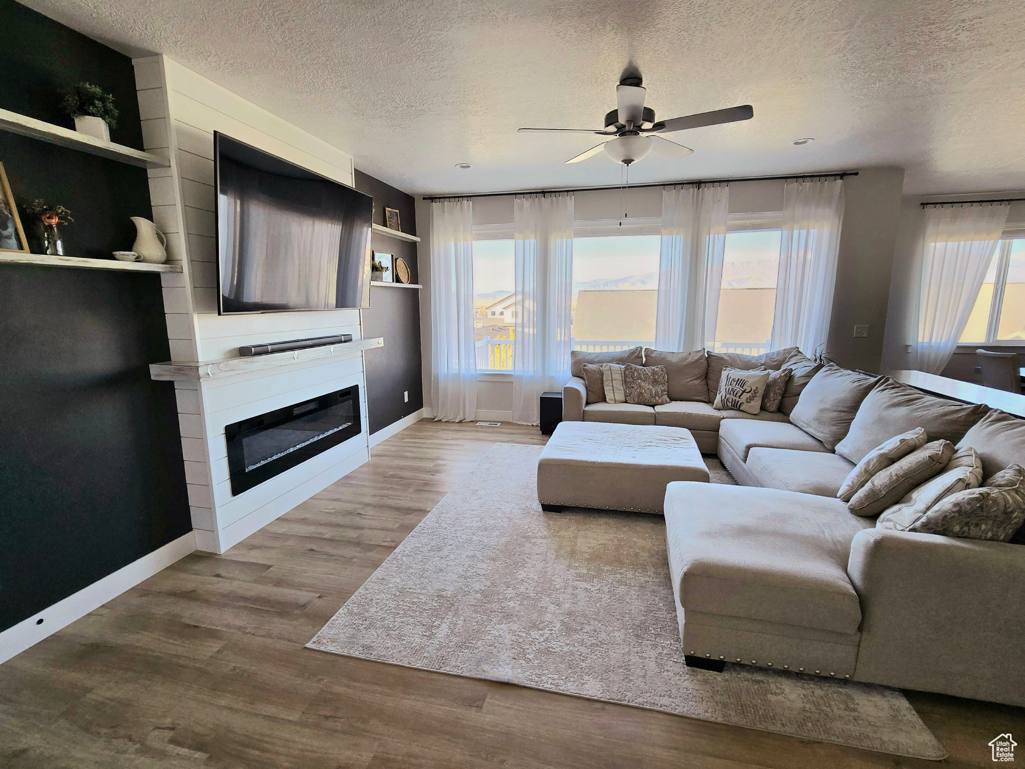 Living room with ceiling fan, a large fireplace, built in features, a textured ceiling, and hardwood / wood-style flooring