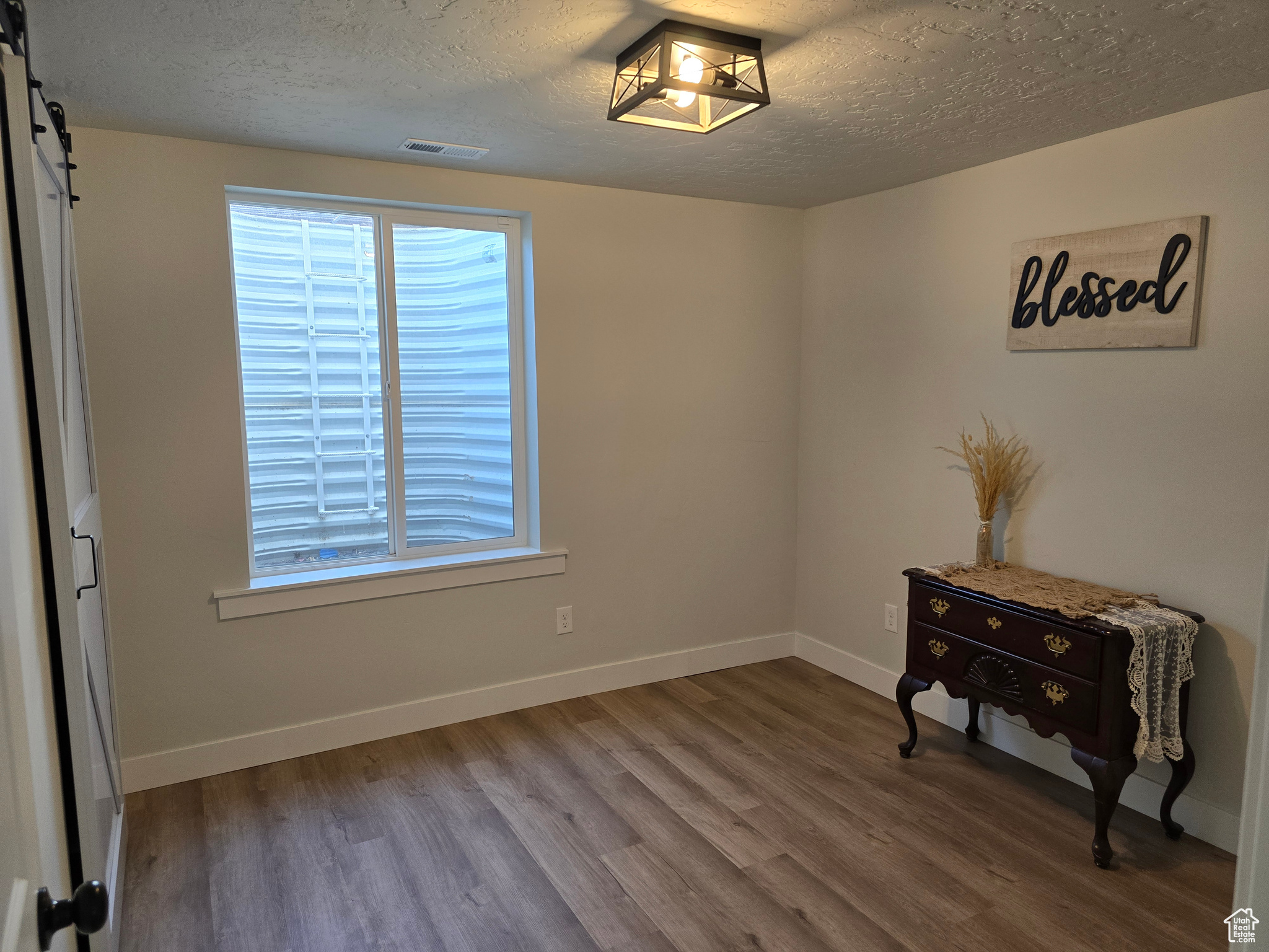 Empty room with a barn door, a textured ceiling, and hardwood / wood-style flooring