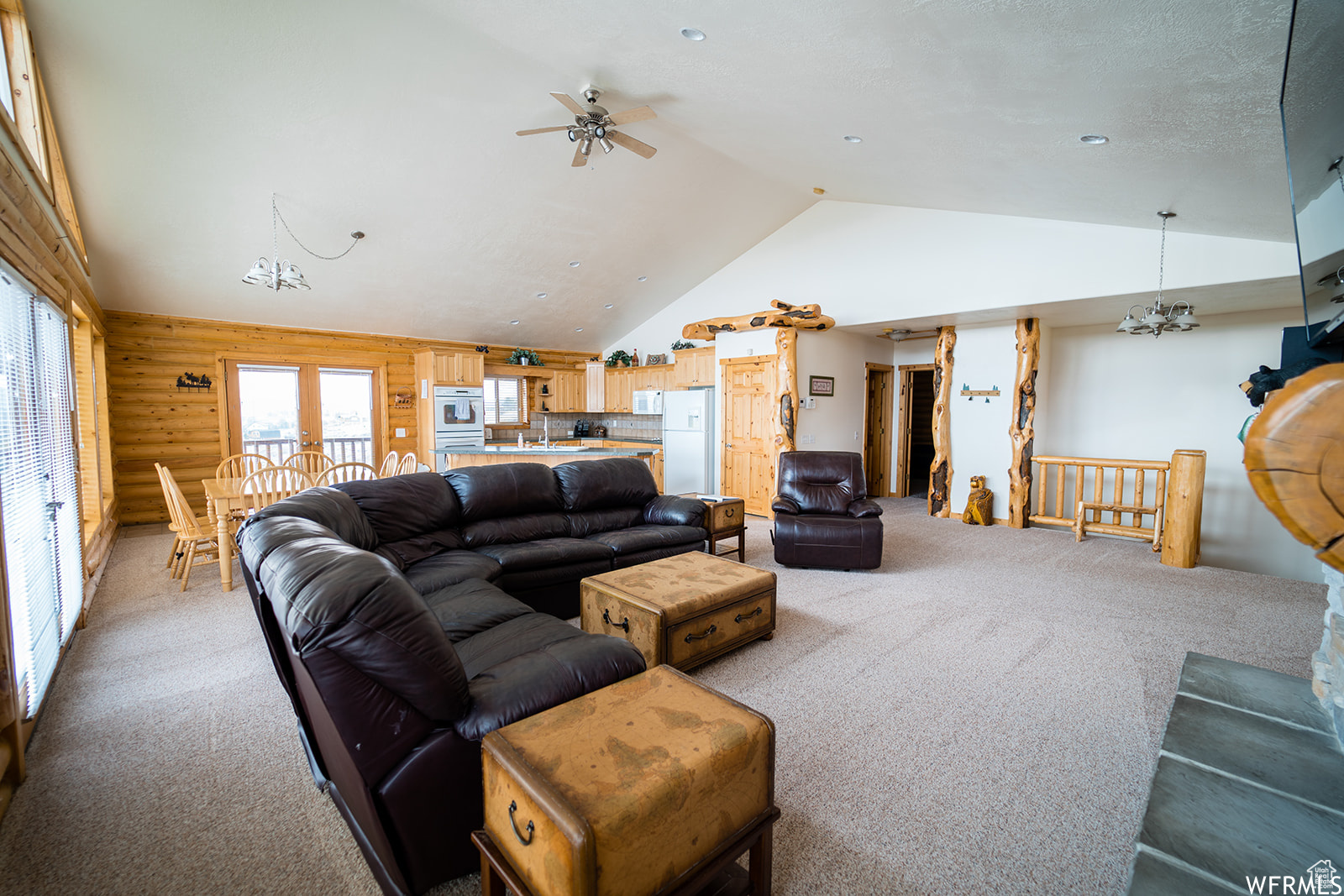 Living room with carpet flooring, log walls, lofted ceiling, wooden walls, and ceiling fan with notable chandelier