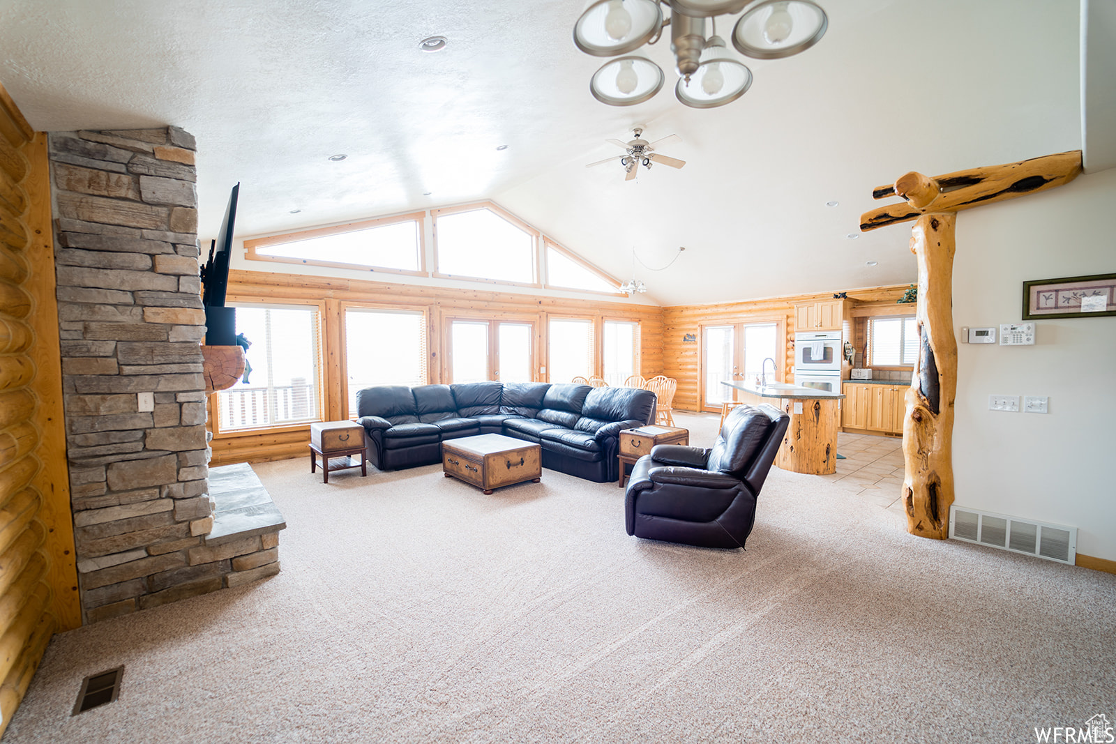 Carpeted living room with a textured ceiling, vaulted ceiling, ceiling fan, sink, and log walls