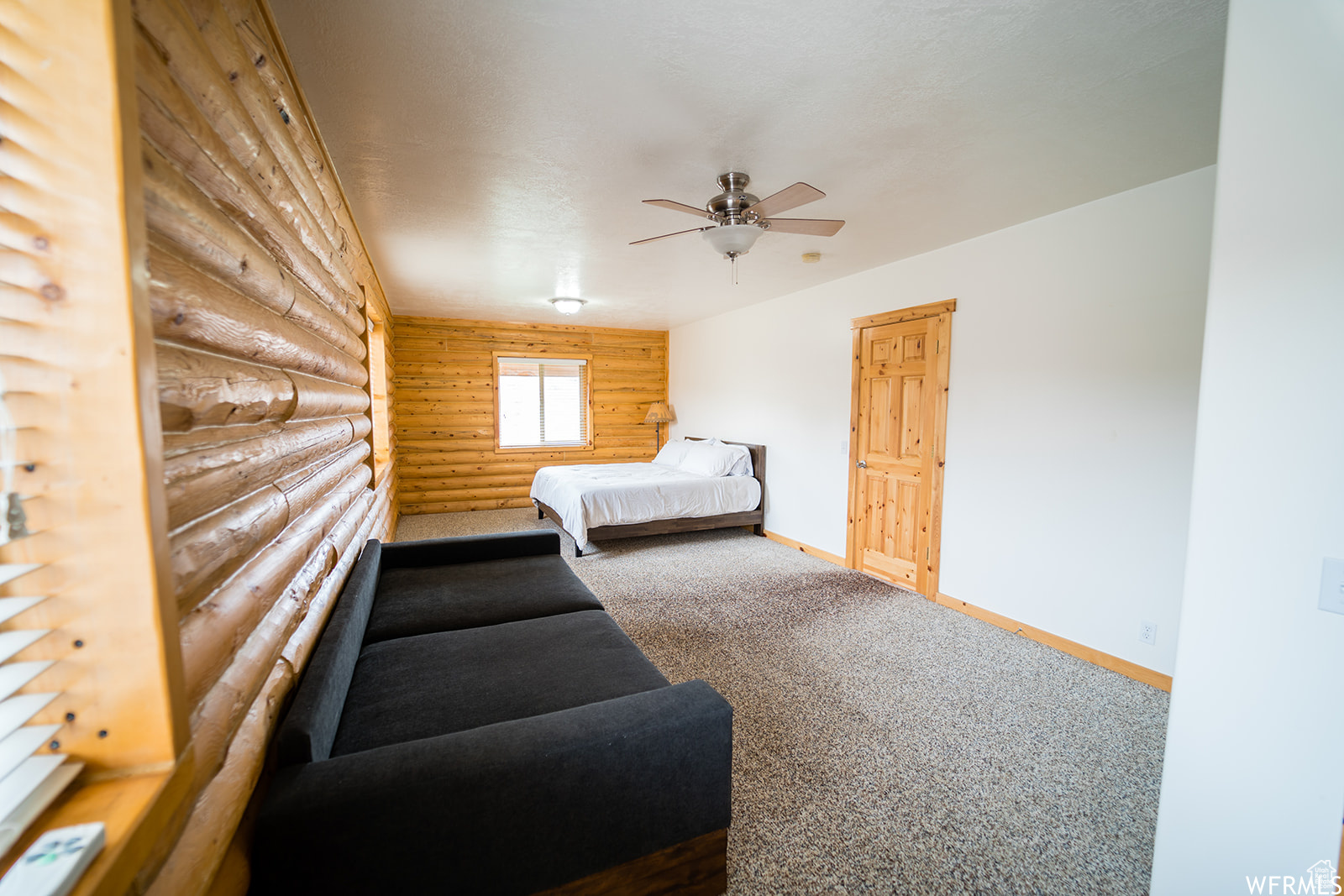 Carpeted bedroom with ceiling fan and log walls