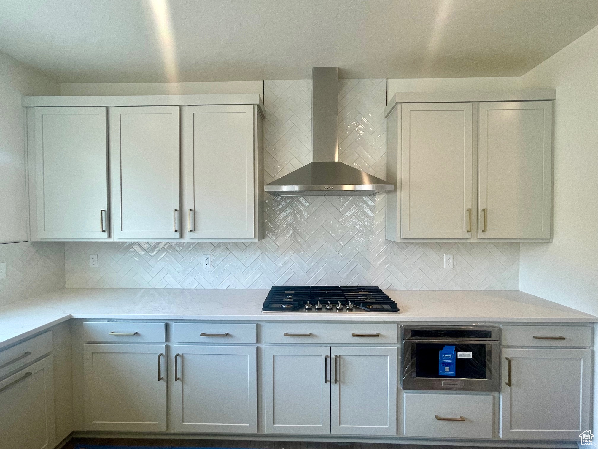 Kitchen with light stone countertops, tasteful backsplash, stainless steel gas cooktop, and wall chimney range hood