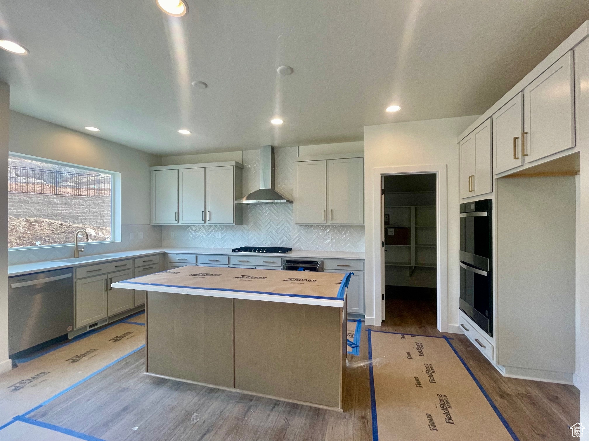 Kitchen featuring a center island, sink, wall chimney range hood, stainless steel dishwasher, and double oven