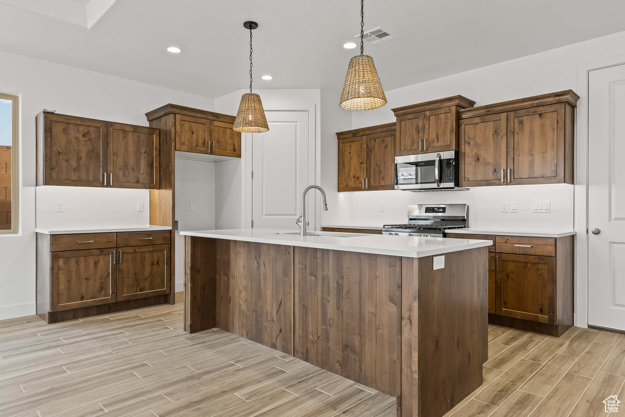 Kitchen featuring sink, stainless steel appliances, hanging light fixtures, and an island with sink