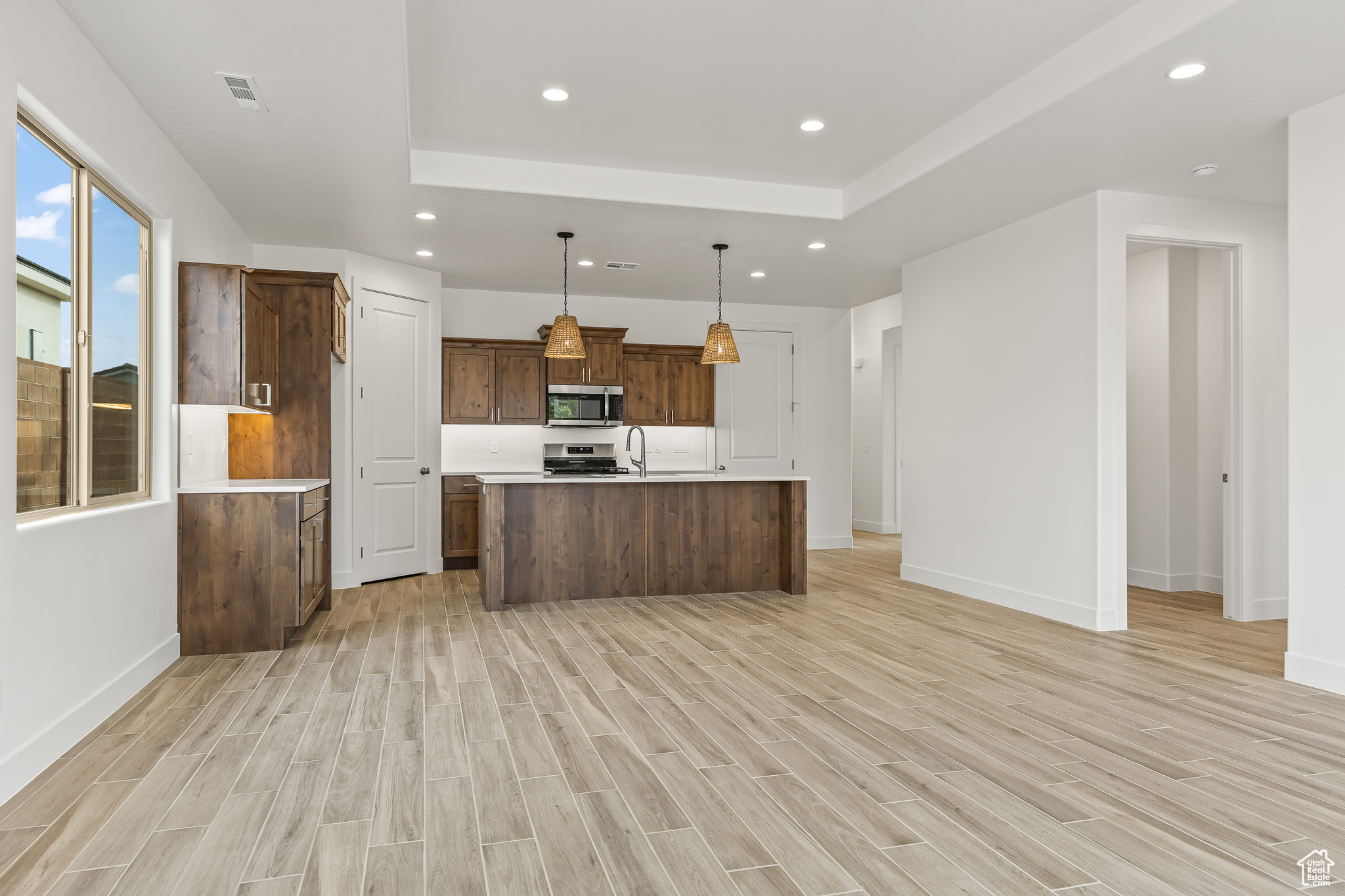 Kitchen featuring range, decorative light fixtures, light hardwood / wood-style flooring, and a kitchen island with sink