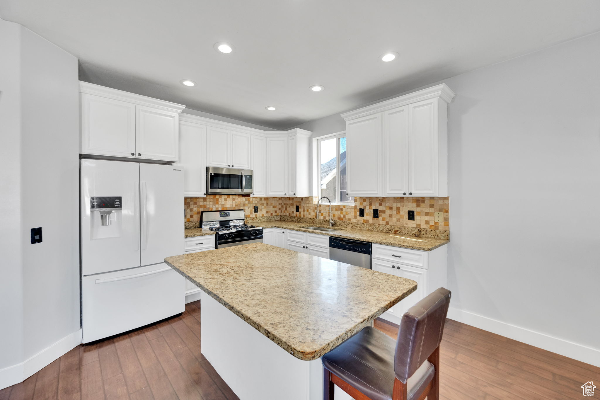 Kitchen featuring appliances with stainless steel finishes, tasteful backsplash, sink, white cabinets, and a center island