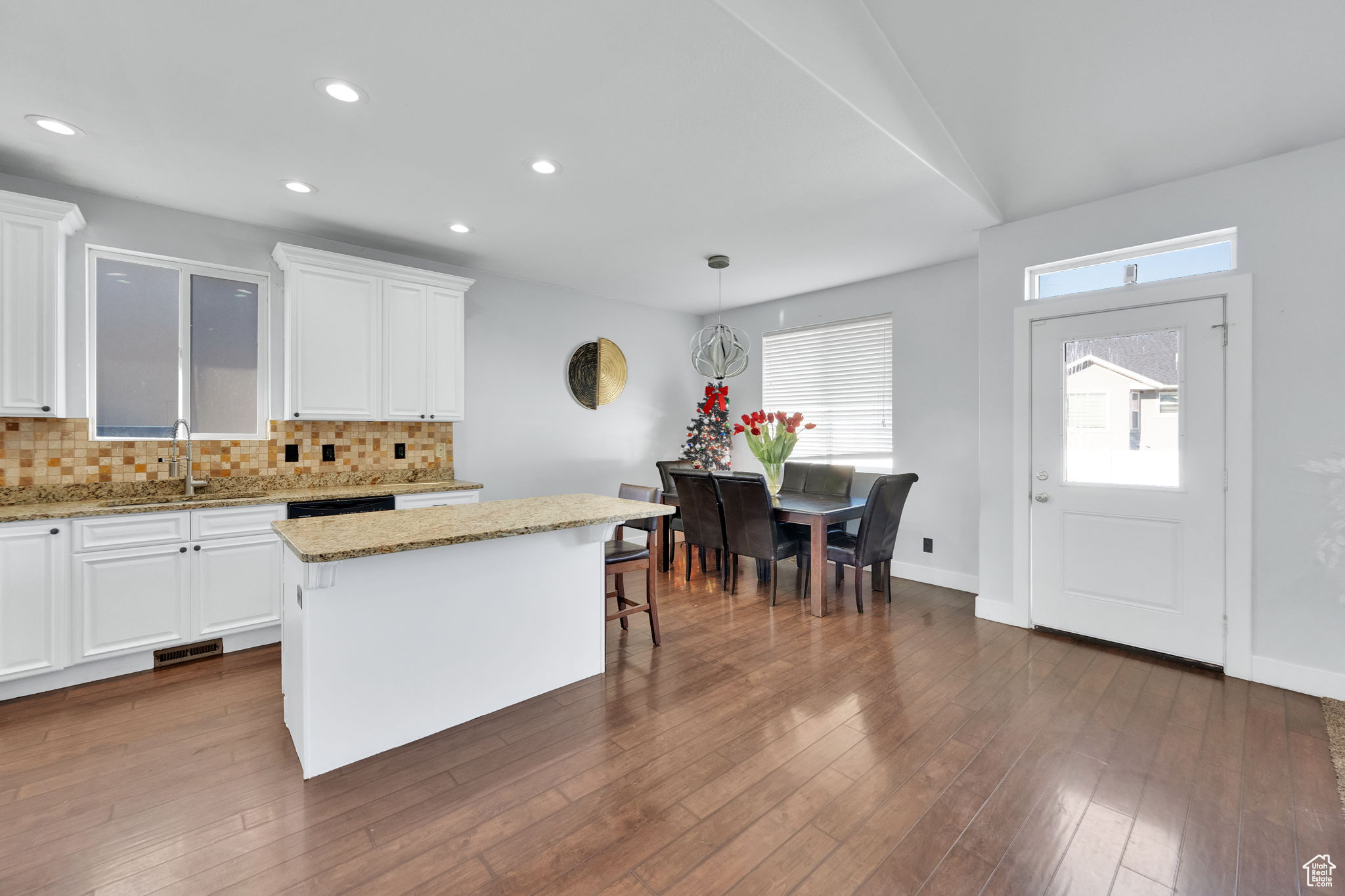 Kitchen with light stone countertops, sink, decorative light fixtures, a center island, and white cabinetry