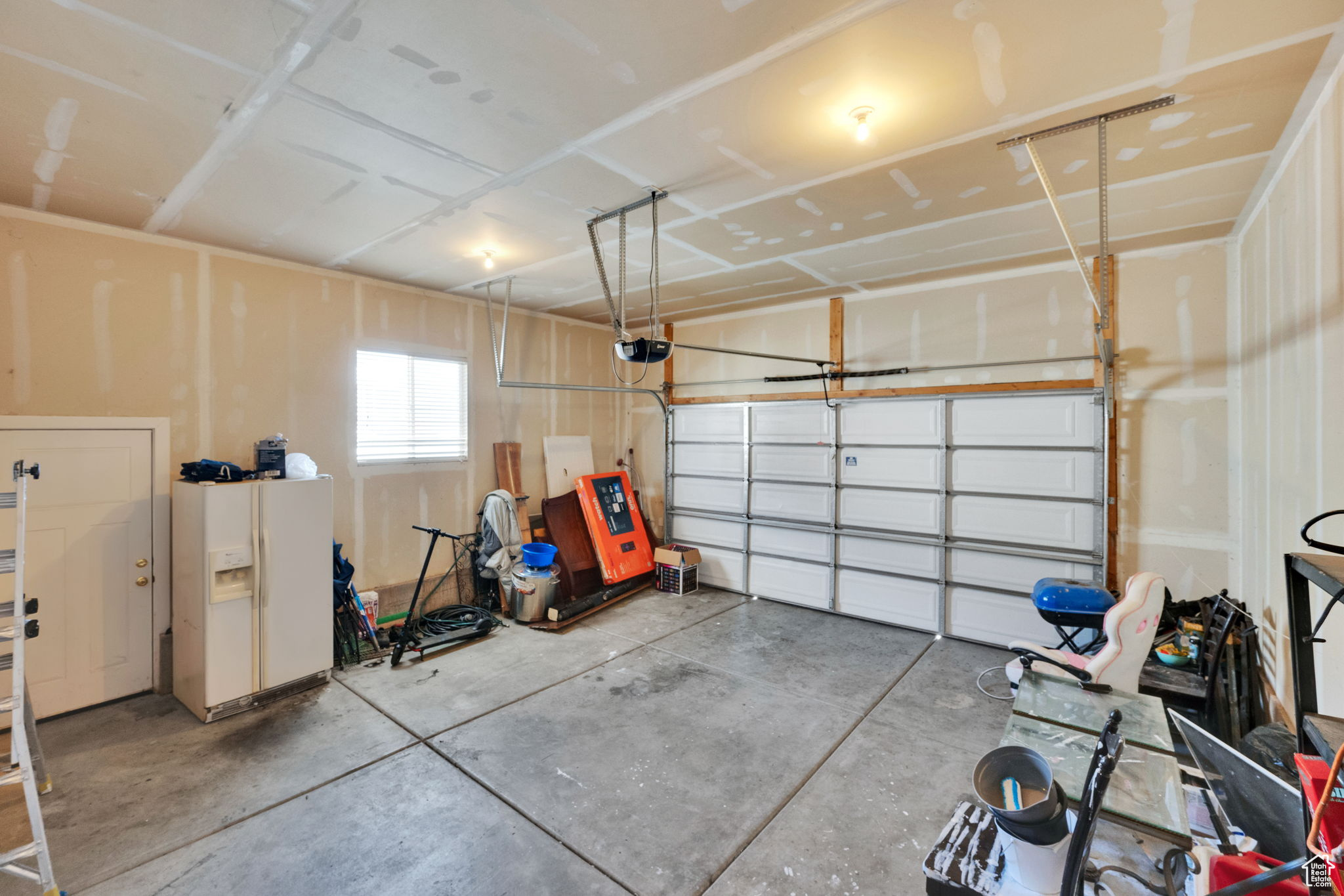 Garage with white refrigerator with ice dispenser and a garage door opener