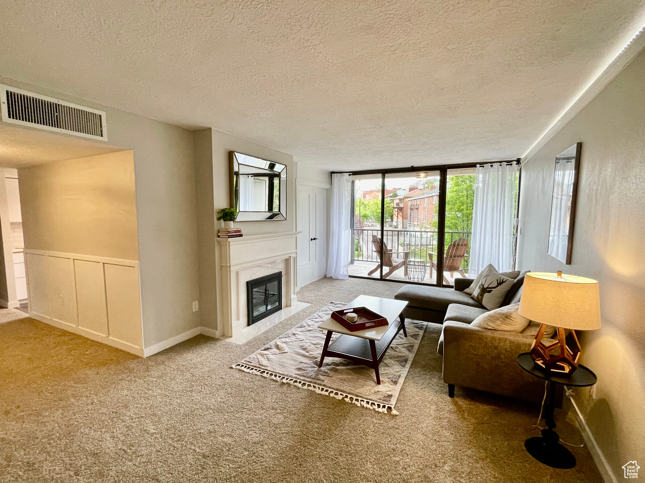 Carpeted living room with a fireplace, a textured ceiling, and a wall of windows