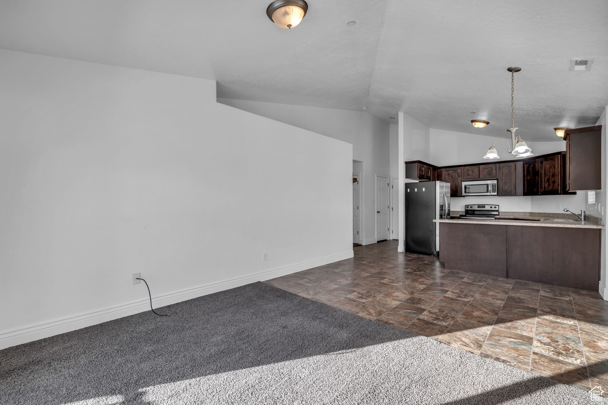 Kitchen with sink, hanging light fixtures, vaulted ceiling, dark brown cabinetry, and stainless steel appliances