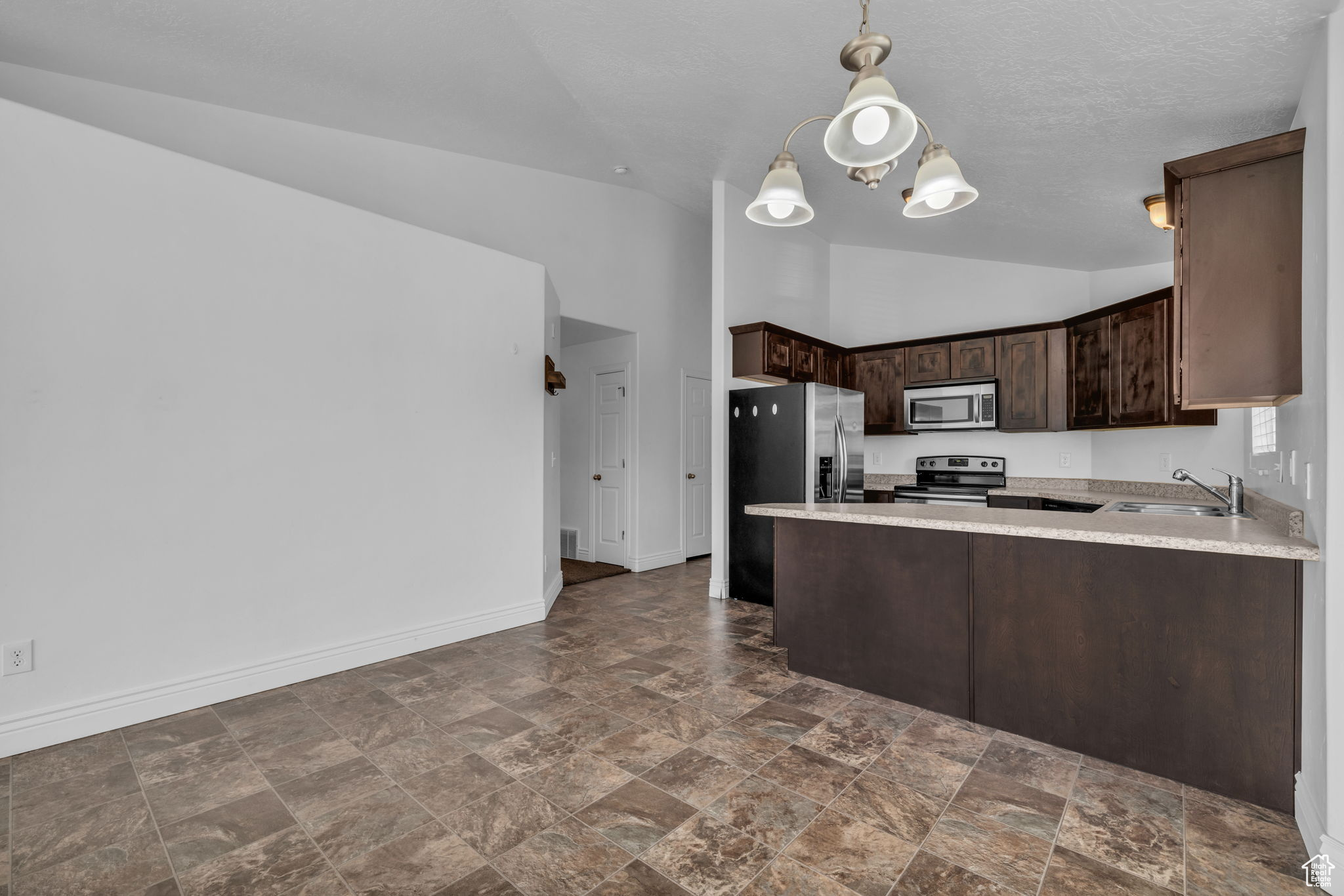 Kitchen featuring kitchen peninsula, dark brown cabinets, stainless steel appliances, sink, and pendant lighting