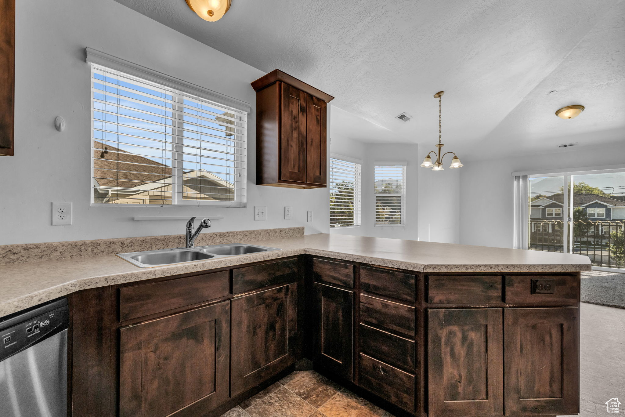 Kitchen with kitchen peninsula, an inviting chandelier, stainless steel dishwasher, and sink