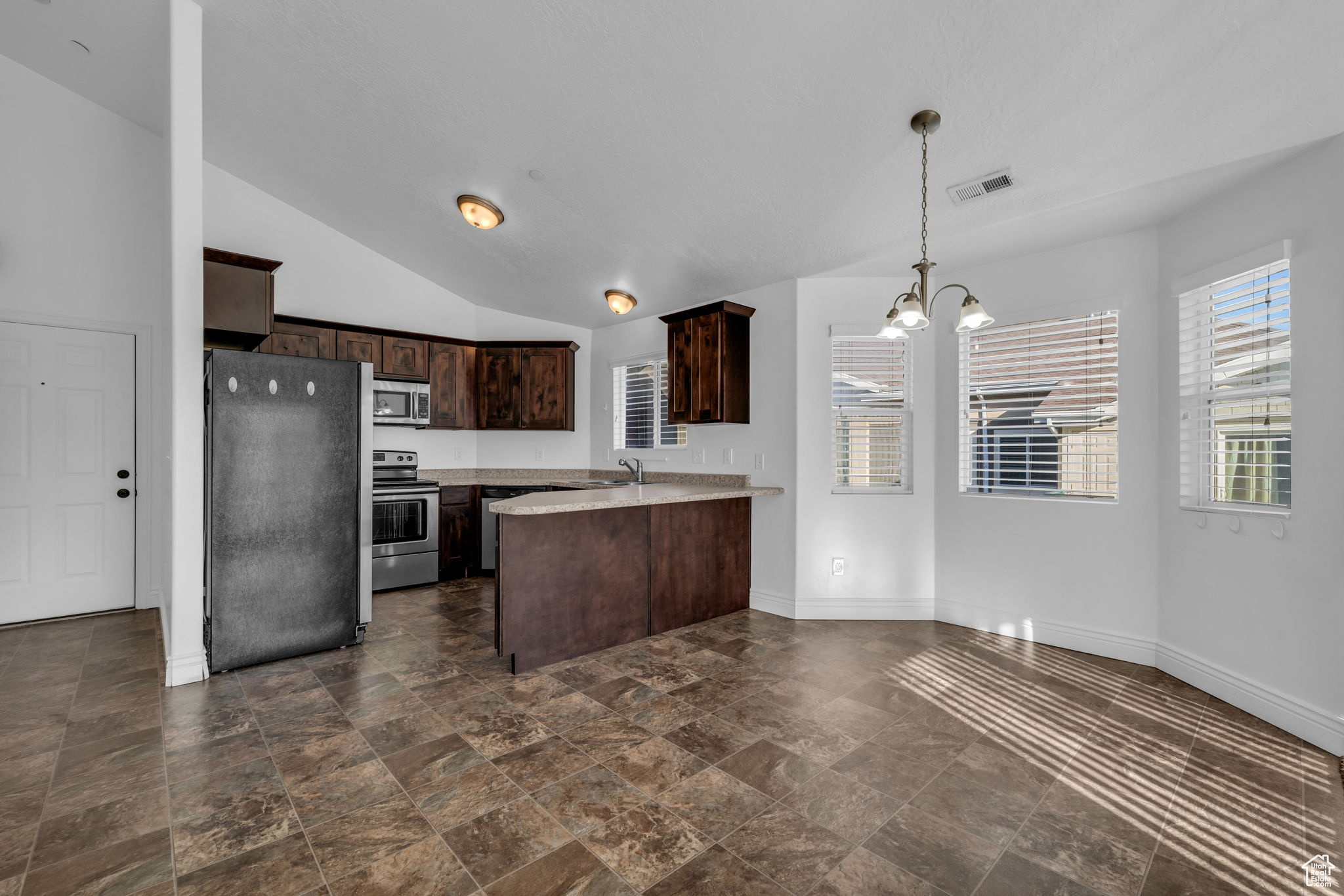 Kitchen with pendant lighting, dark brown cabinetry, a notable chandelier, kitchen peninsula, and stainless steel appliances