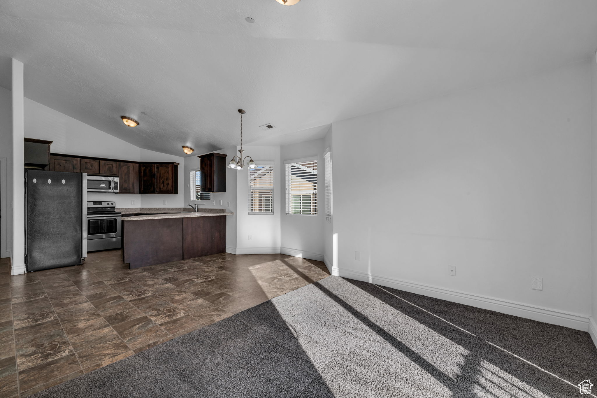 Kitchen with appliances with stainless steel finishes, dark brown cabinetry, vaulted ceiling, decorative light fixtures, and a notable chandelier