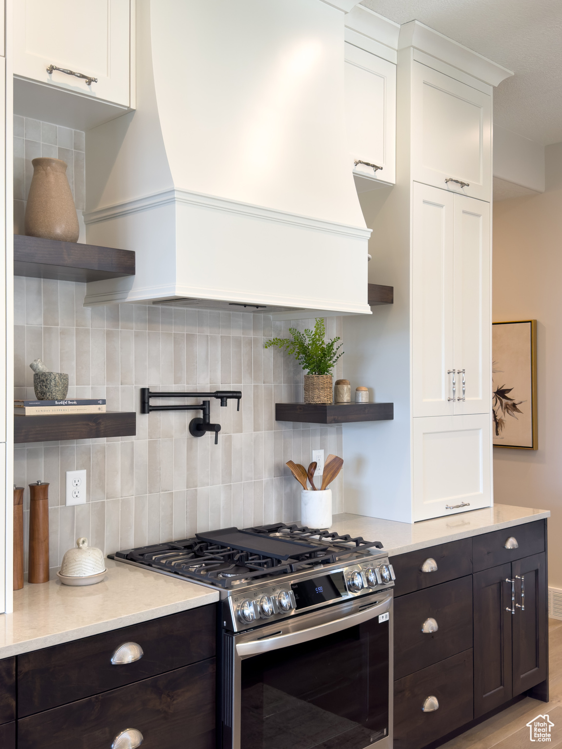 Kitchen with tasteful backsplash, dark brown cabinetry, white cabinets, and stainless steel gas range