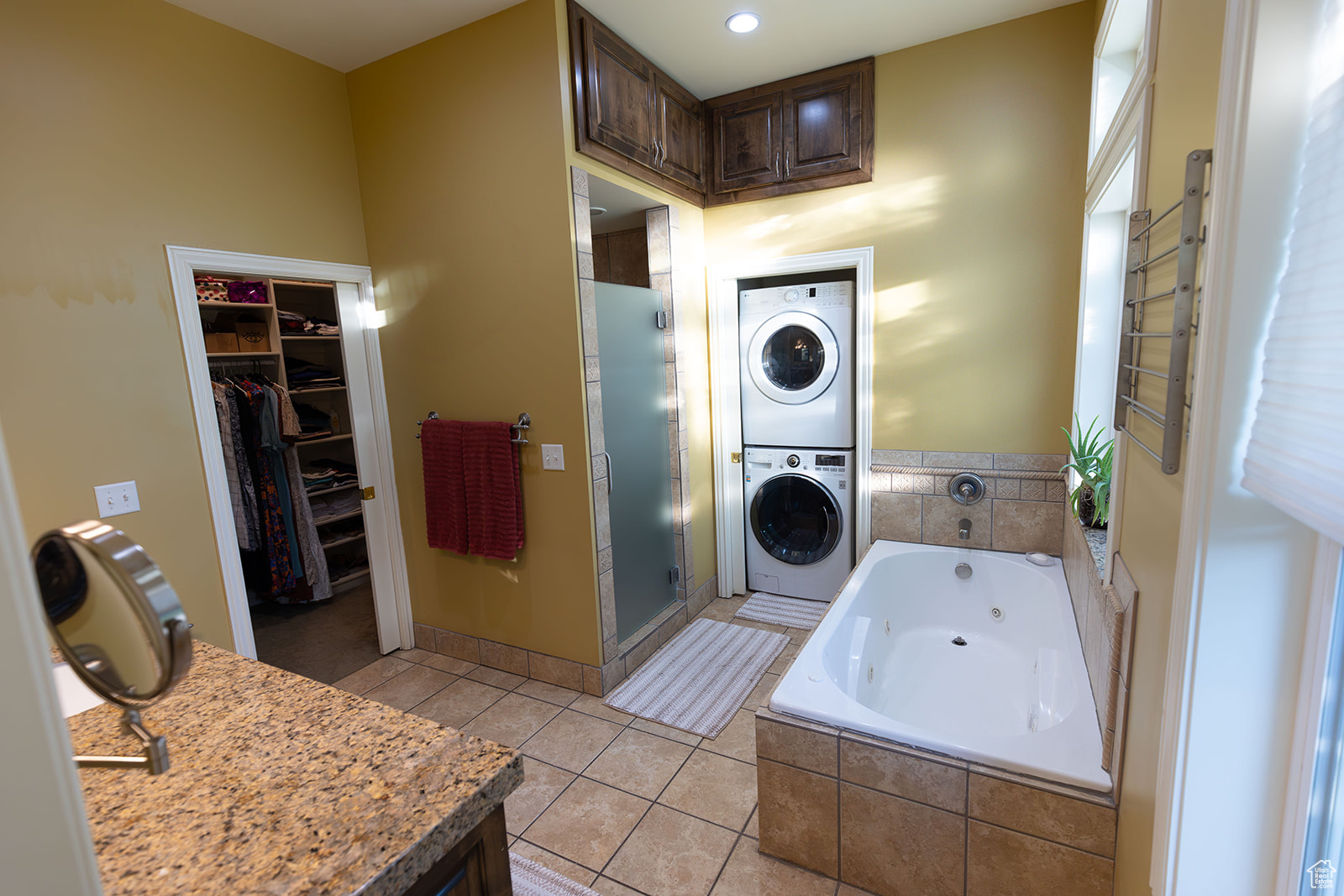 Bathroom with tile patterned flooring, stacked washer / drying machine, and plus walk in shower