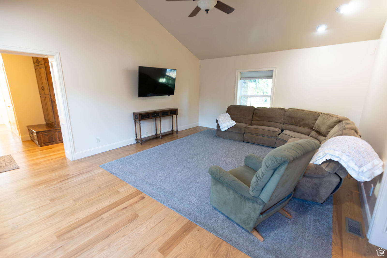 Living room with ceiling fan, high vaulted ceiling, and light wood-type flooring