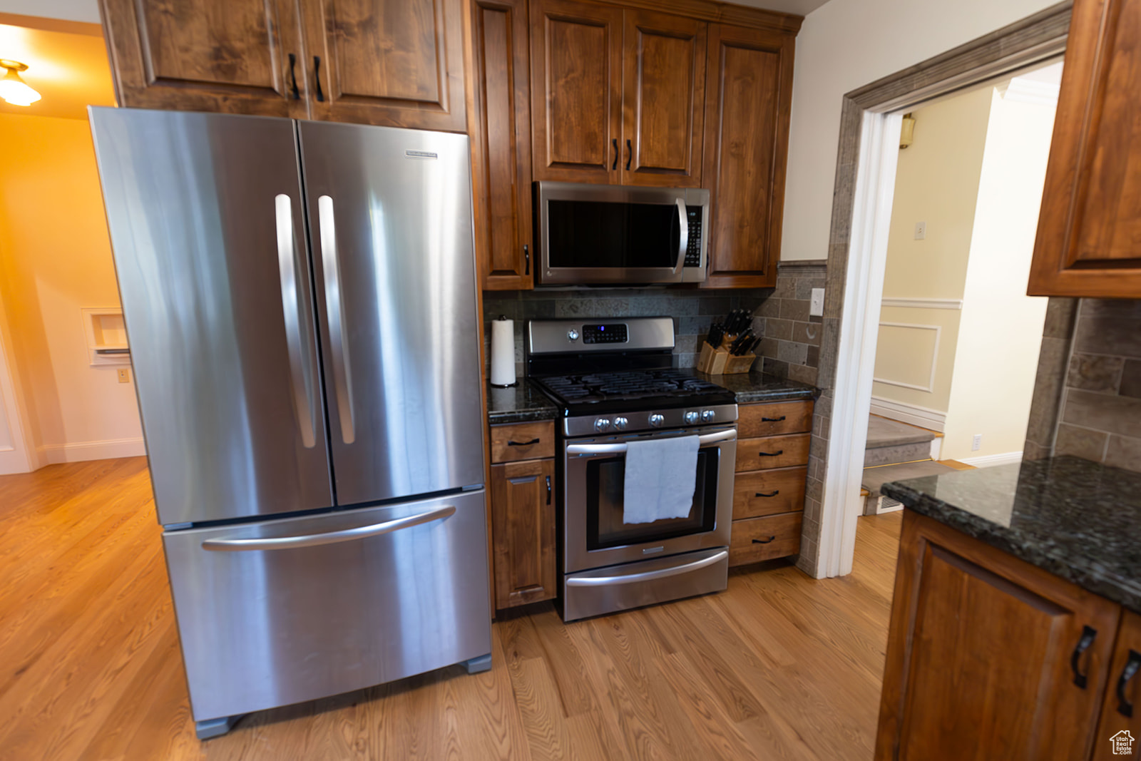 Kitchen with backsplash, light wood-type flooring, stainless steel appliances, and dark stone counters