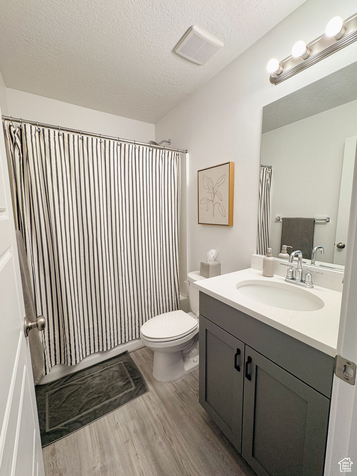 Full bathroom with shower / bath combo with shower curtain, hardwood / wood-style floors, vanity, and a textured ceiling