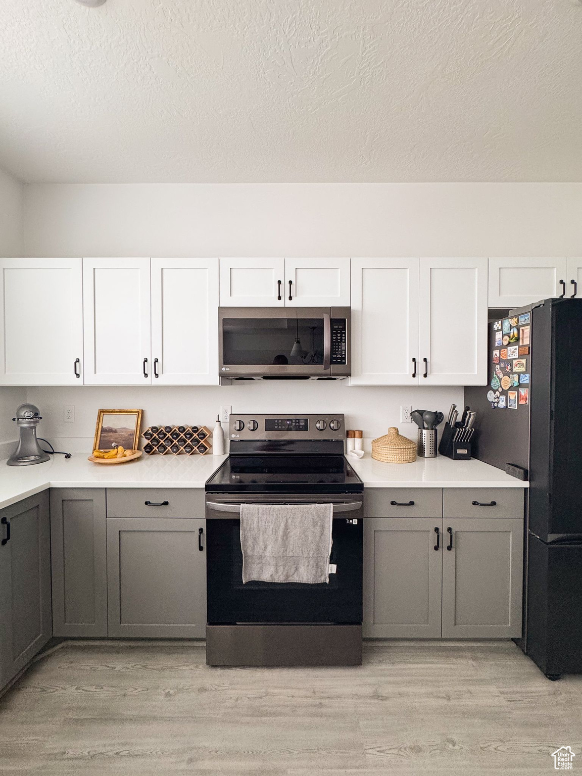 Kitchen featuring gray cabinetry, light hardwood / wood-style flooring, a textured ceiling, appliances with stainless steel finishes, and white cabinetry