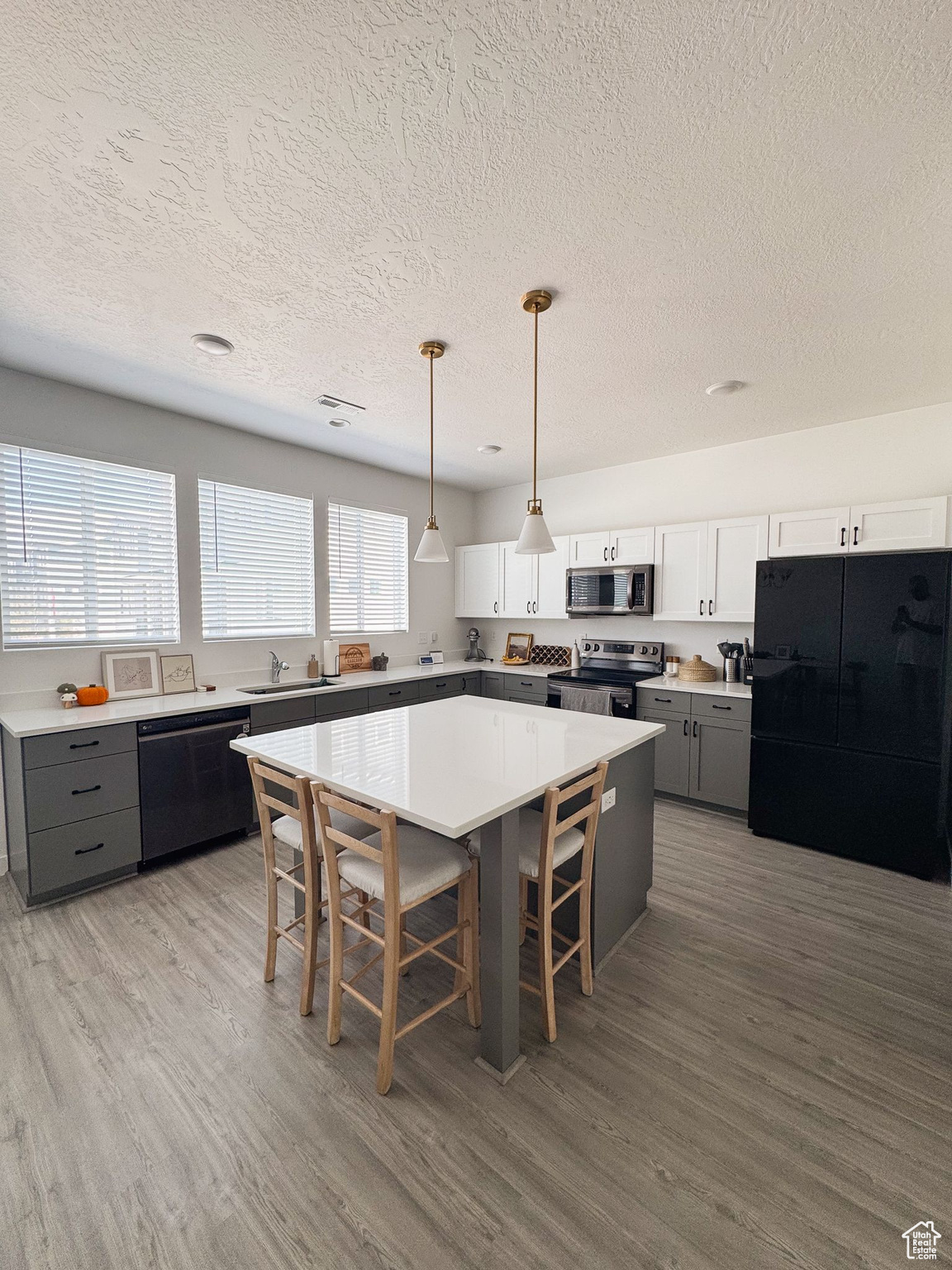 Kitchen featuring gray cabinetry, white cabinetry, pendant lighting, a kitchen island, and black appliances