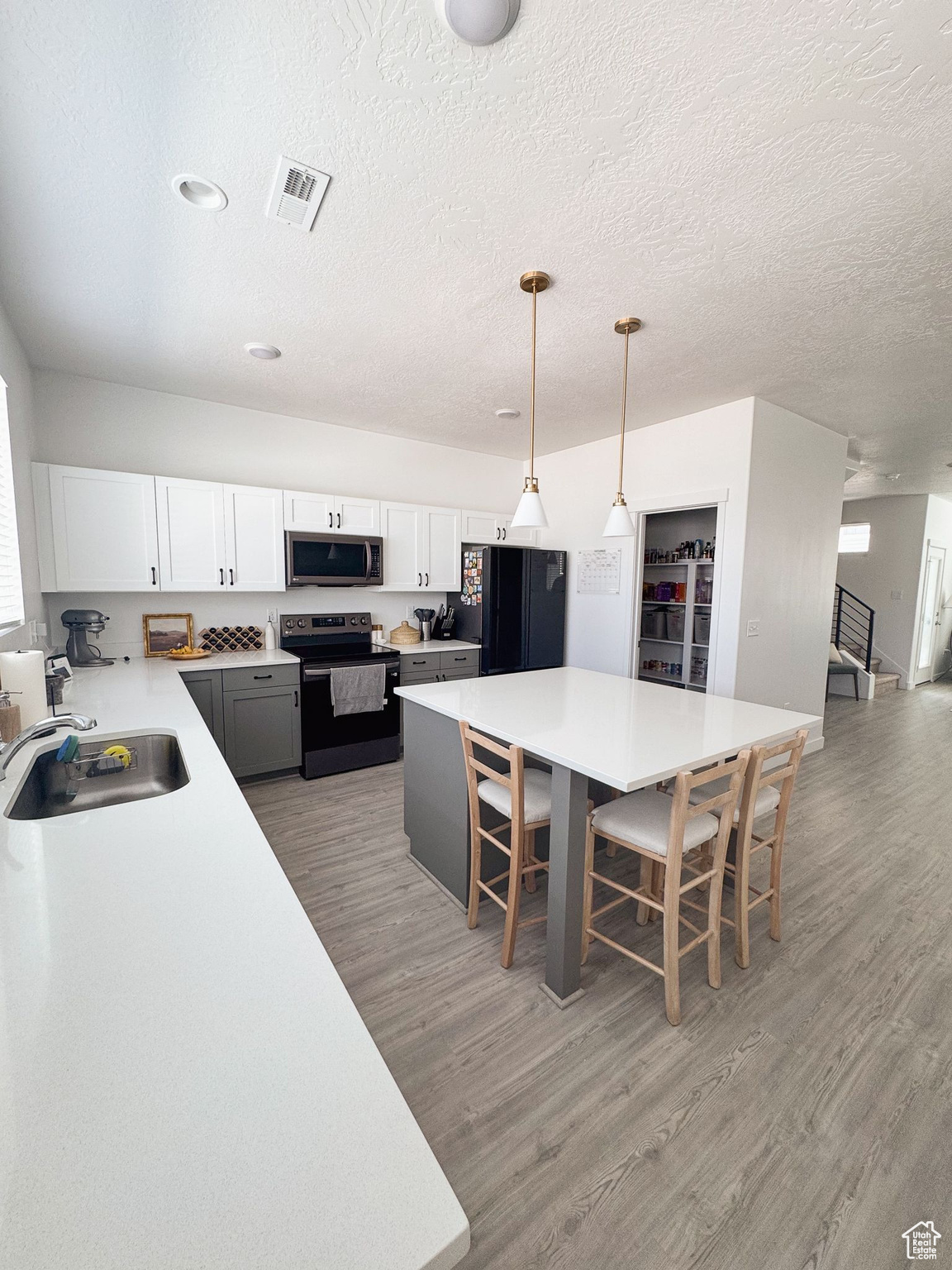 Kitchen featuring a kitchen breakfast bar, white cabinetry, hanging light fixtures, and black appliances