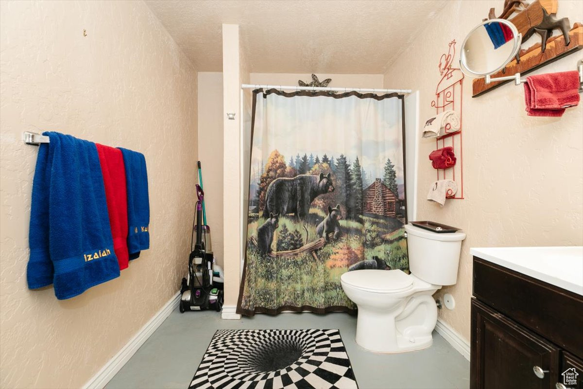 Bathroom with a textured ceiling, vanity, toilet, and concrete floors