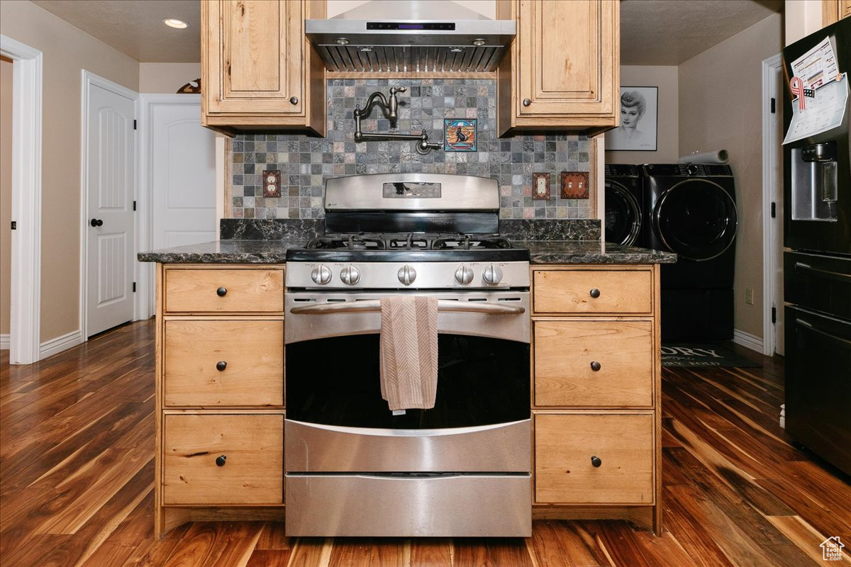 Kitchen with light brown cabinetry, dark stone counters, extractor fan, separate washer and dryer, and stainless steel range with gas cooktop