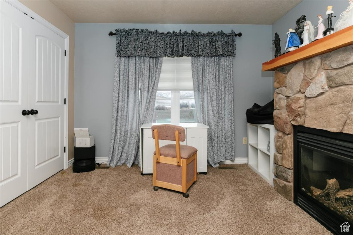 Sitting room with carpet flooring, a stone fireplace, and a textured ceiling