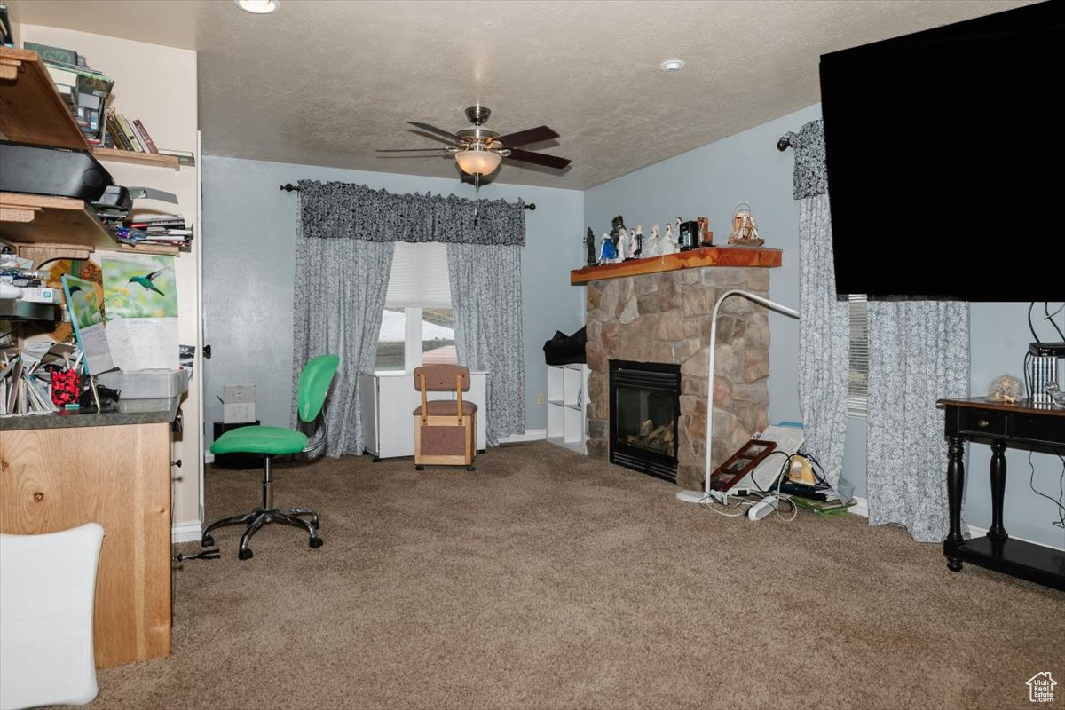 Office space featuring a fireplace, a textured ceiling, carpet floors, and ceiling fan