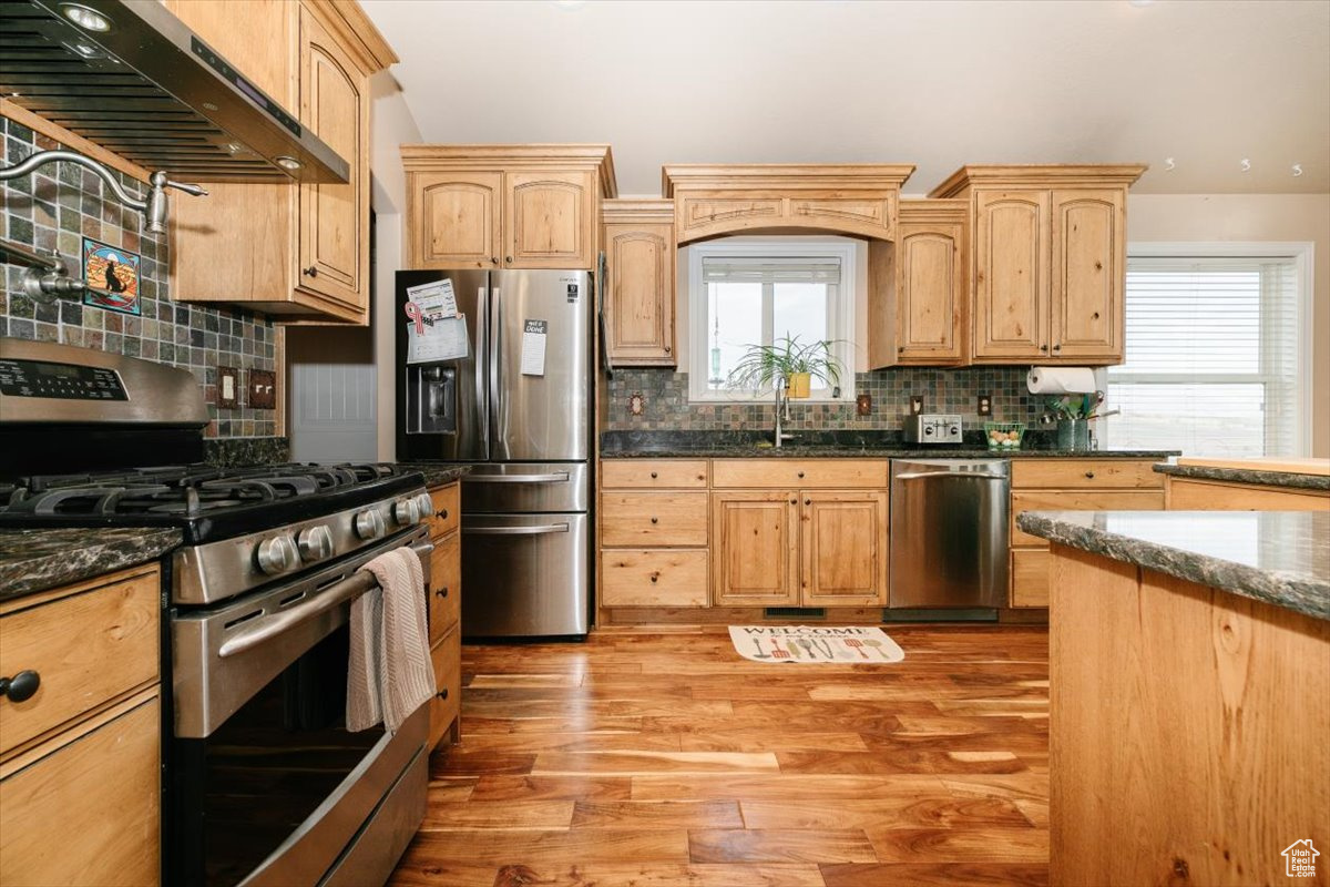 Kitchen featuring light wood-type flooring, stainless steel appliances, extractor fan, sink, and dark stone countertops