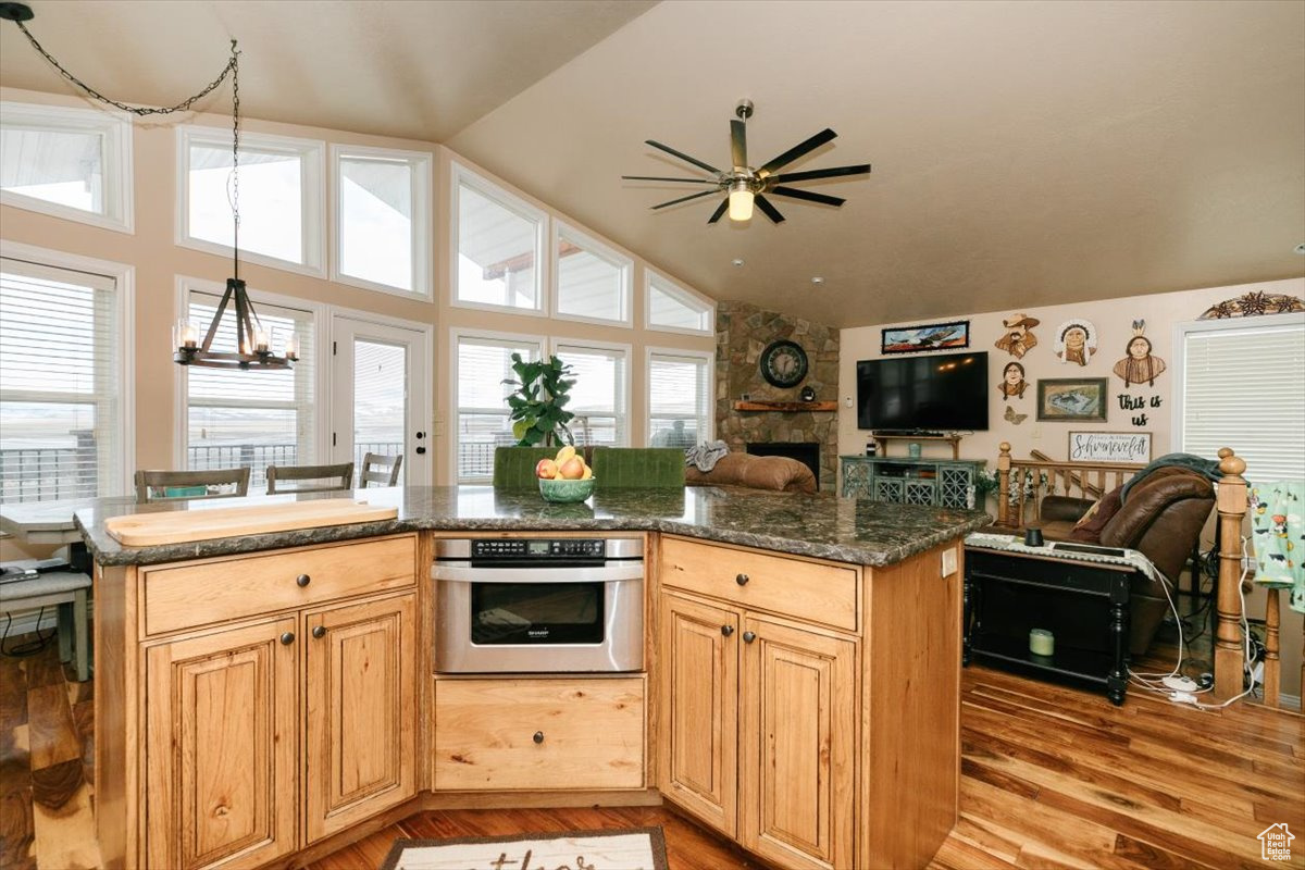 Kitchen with stainless steel oven, vaulted ceiling, a fireplace, ceiling fan with notable chandelier, and light wood-type flooring