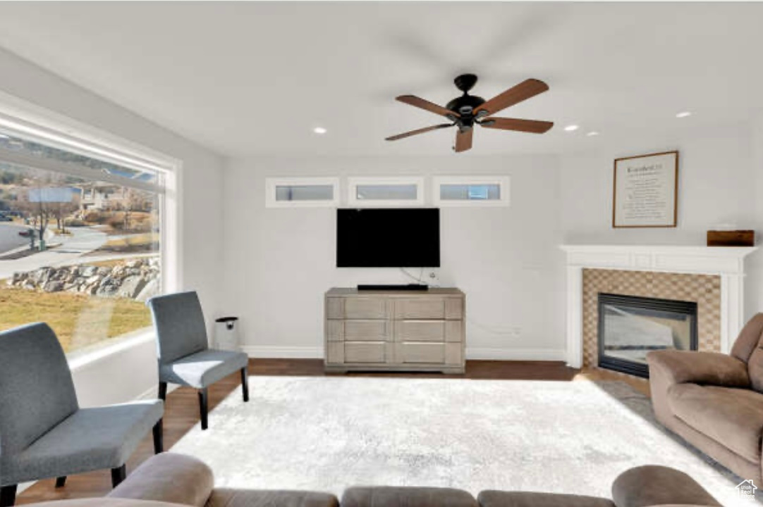 Living room with ceiling fan, wood-type flooring, and a tiled fireplace