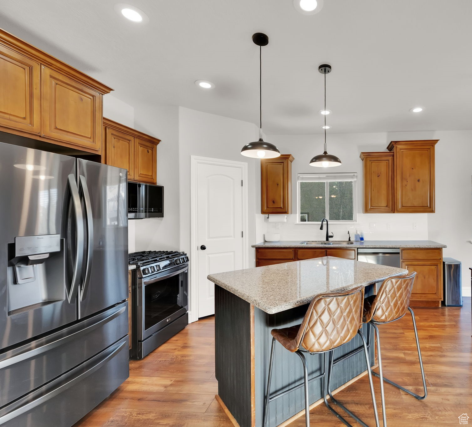 Kitchen with black gas range, sink, stainless steel fridge with ice dispenser, decorative light fixtures, and a kitchen island