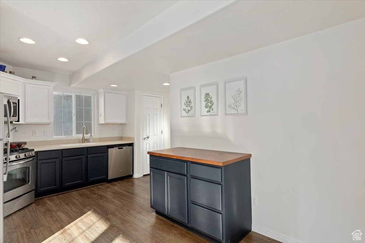 Kitchen with wood counters, stainless steel appliances, dark wood-type flooring, sink, and white cabinets