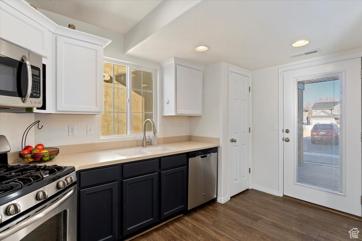 Kitchen with dark hardwood / wood-style floors, white cabinetry, sink, and appliances with stainless steel finishes