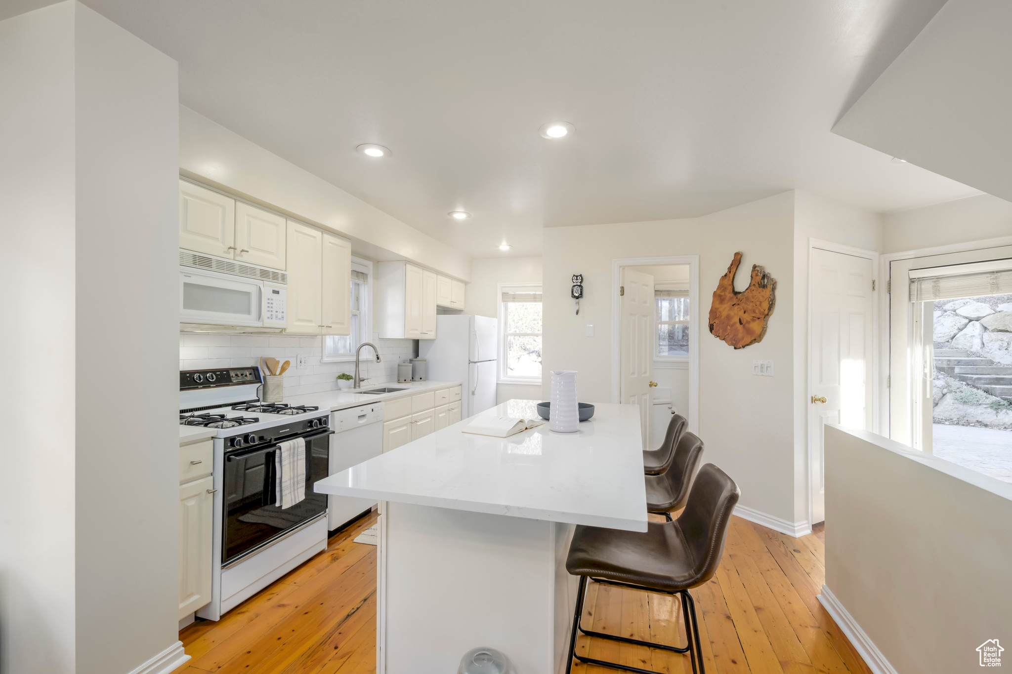 Kitchen with white appliances, sink, a kitchen island, a kitchen bar, and white cabinetry