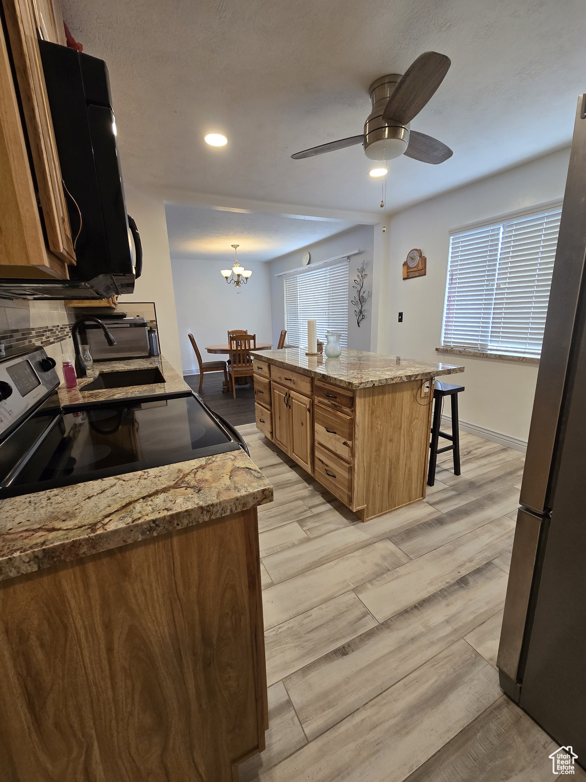 Kitchen featuring stove, ceiling fan with notable chandelier, hanging light fixtures, stainless steel fridge, and light wood-type flooring