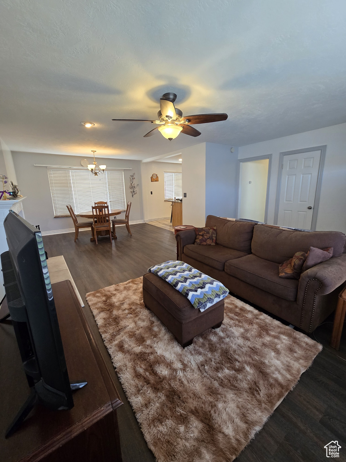 Living room with ceiling fan with notable chandelier and dark hardwood / wood-style flooring