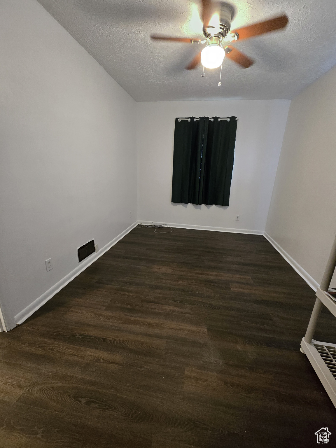 Spare room featuring ceiling fan, dark wood-type flooring, and a textured ceiling