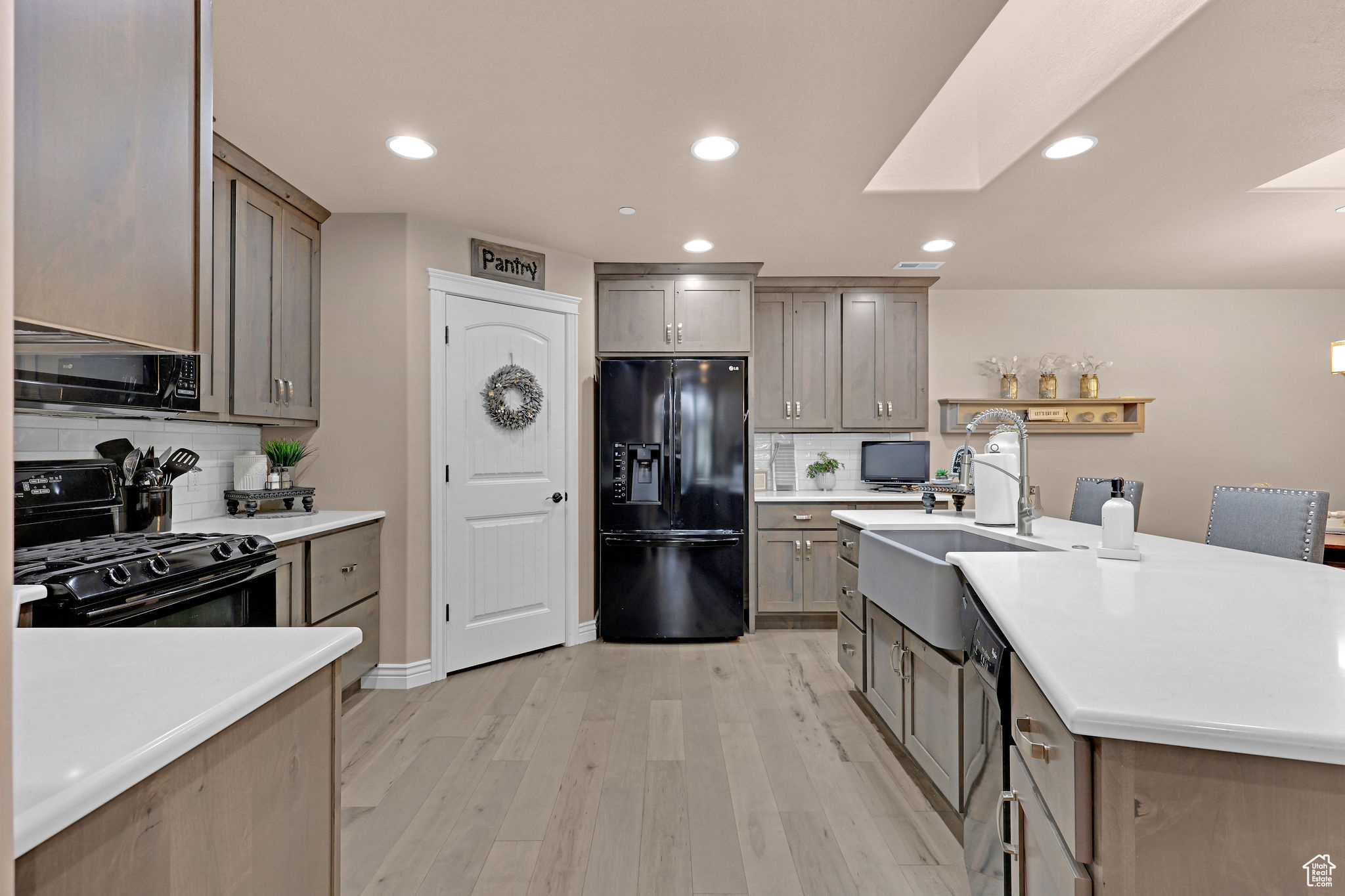 Kitchen with backsplash, black appliances, sink, a skylight, and light hardwood / wood-style flooring