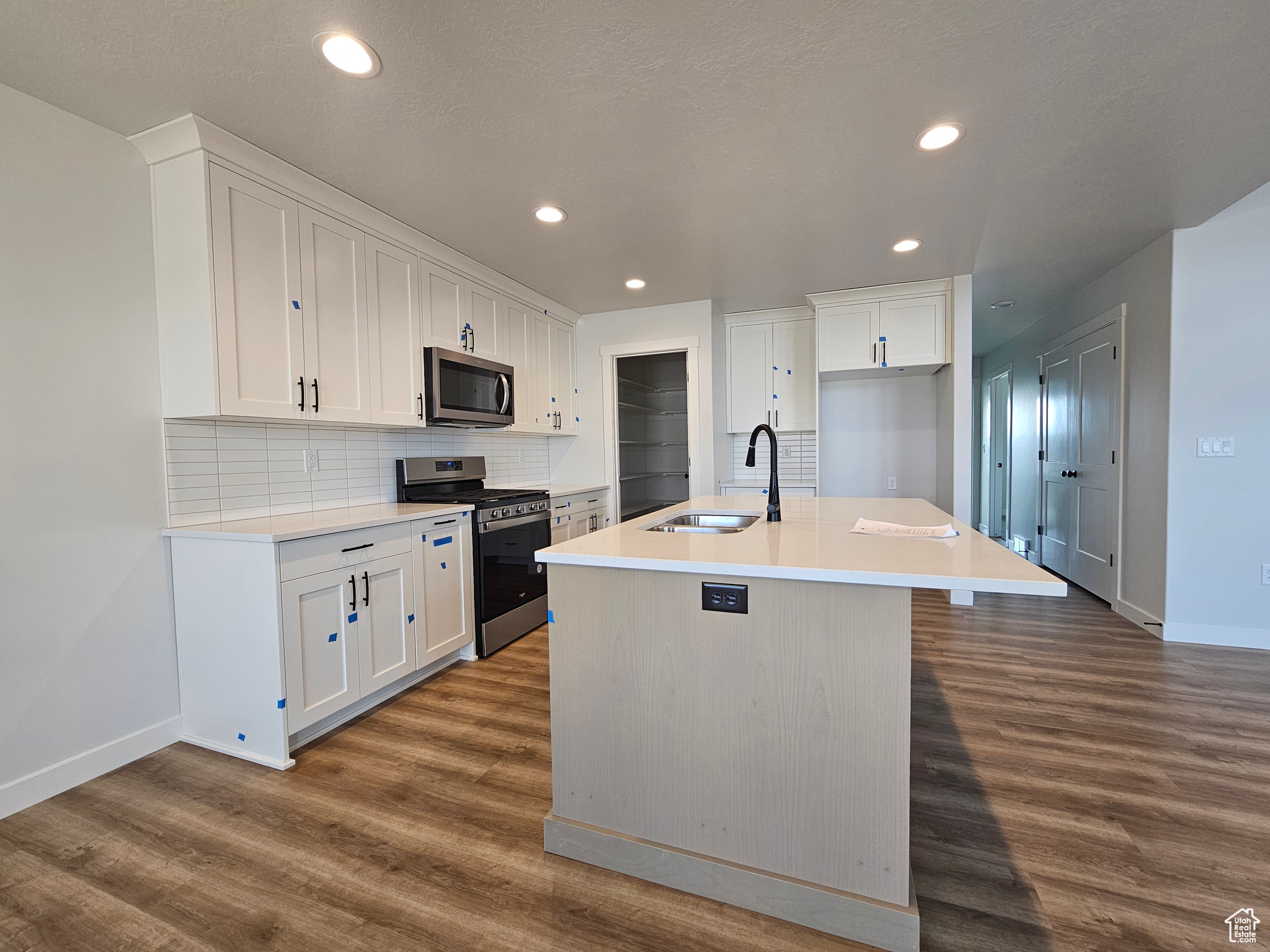 Kitchen with a kitchen island with sink, sink, hardwood / wood-style flooring, white cabinetry, and stainless steel appliances