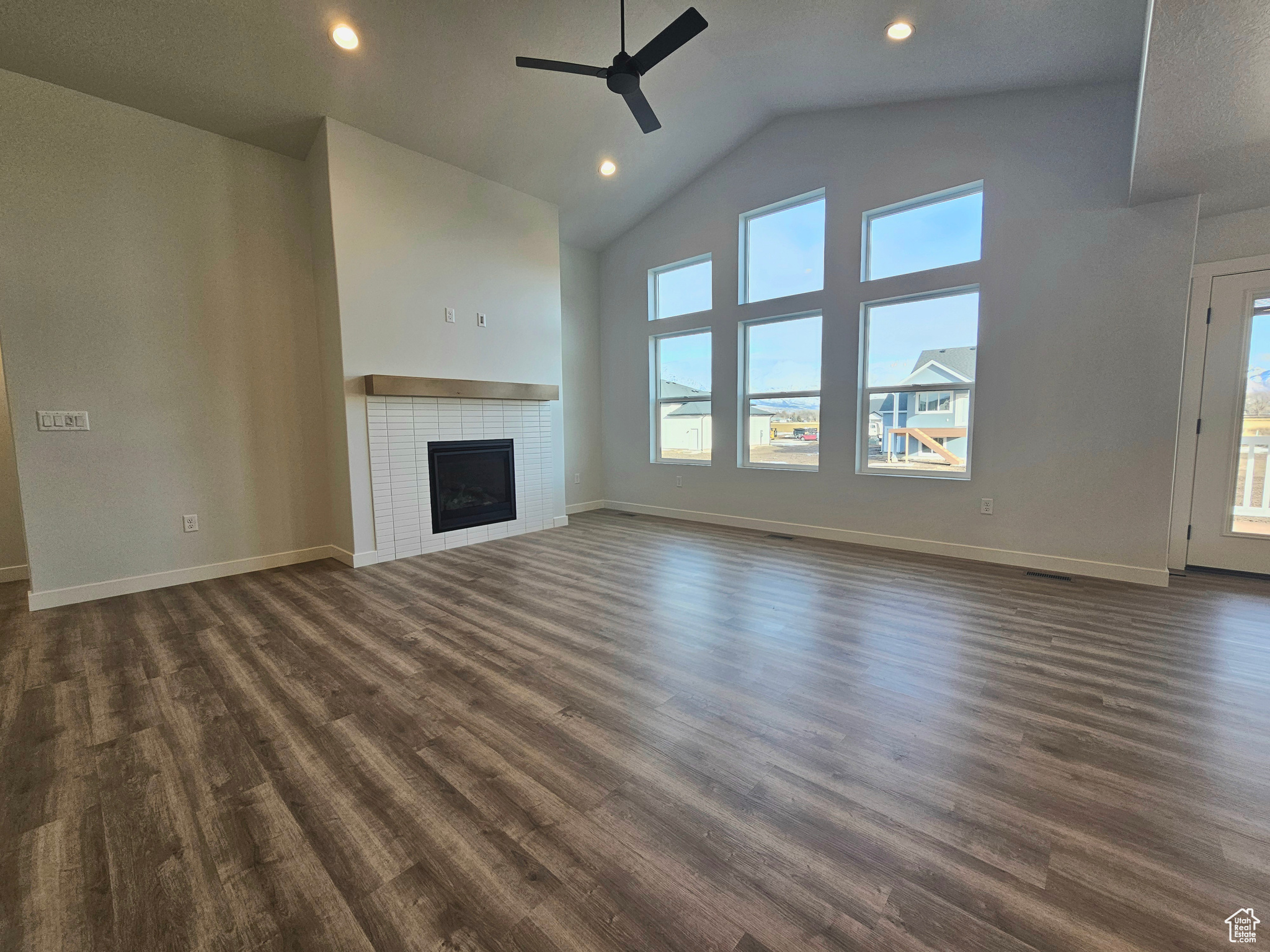 Unfurnished living room featuring dark hardwood / wood-style floors, a brick fireplace, ceiling fan, and a healthy amount of sunlight