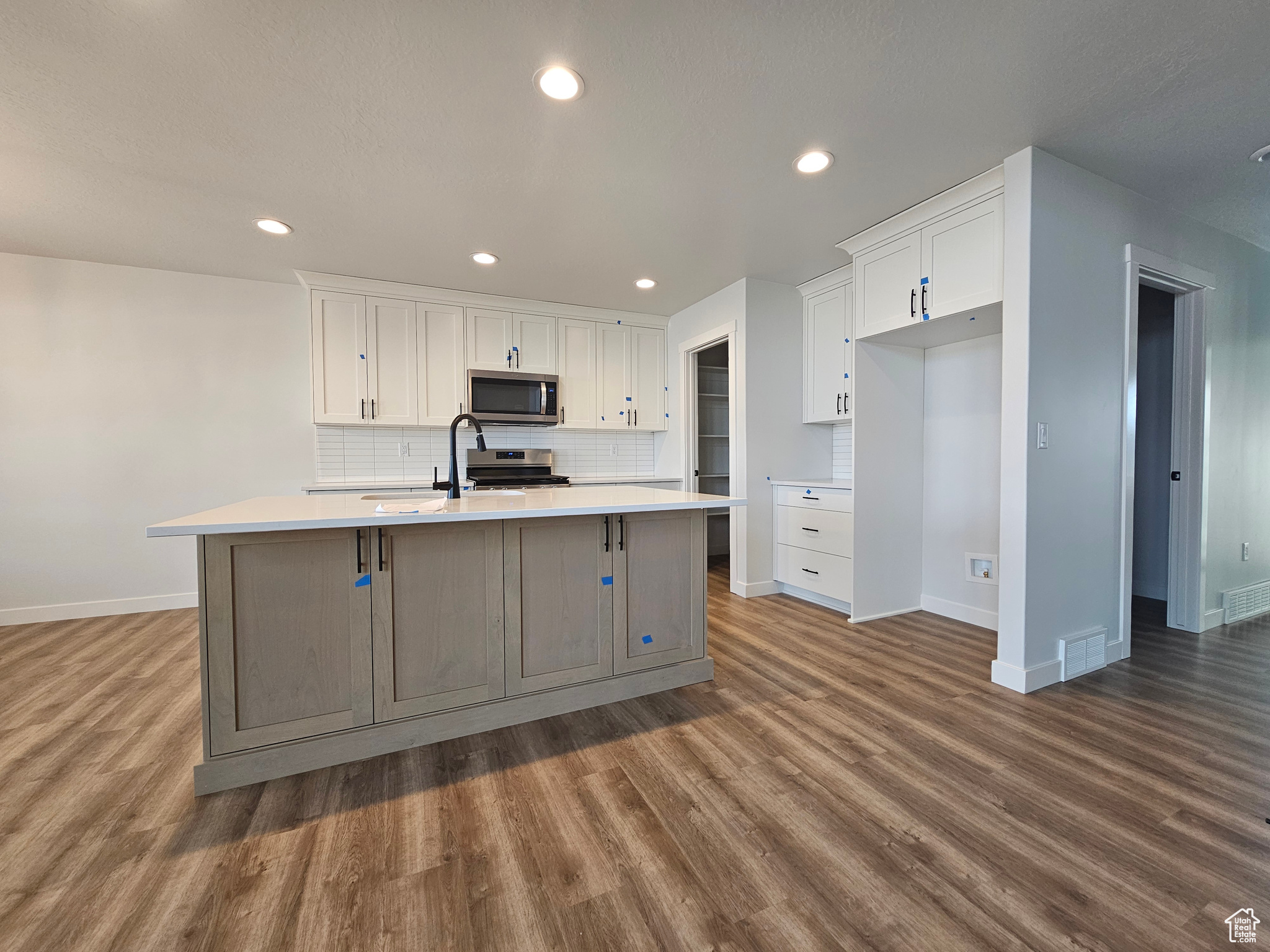 Kitchen with tasteful backsplash, white cabinetry, an island with sink, and appliances with stainless steel finishes