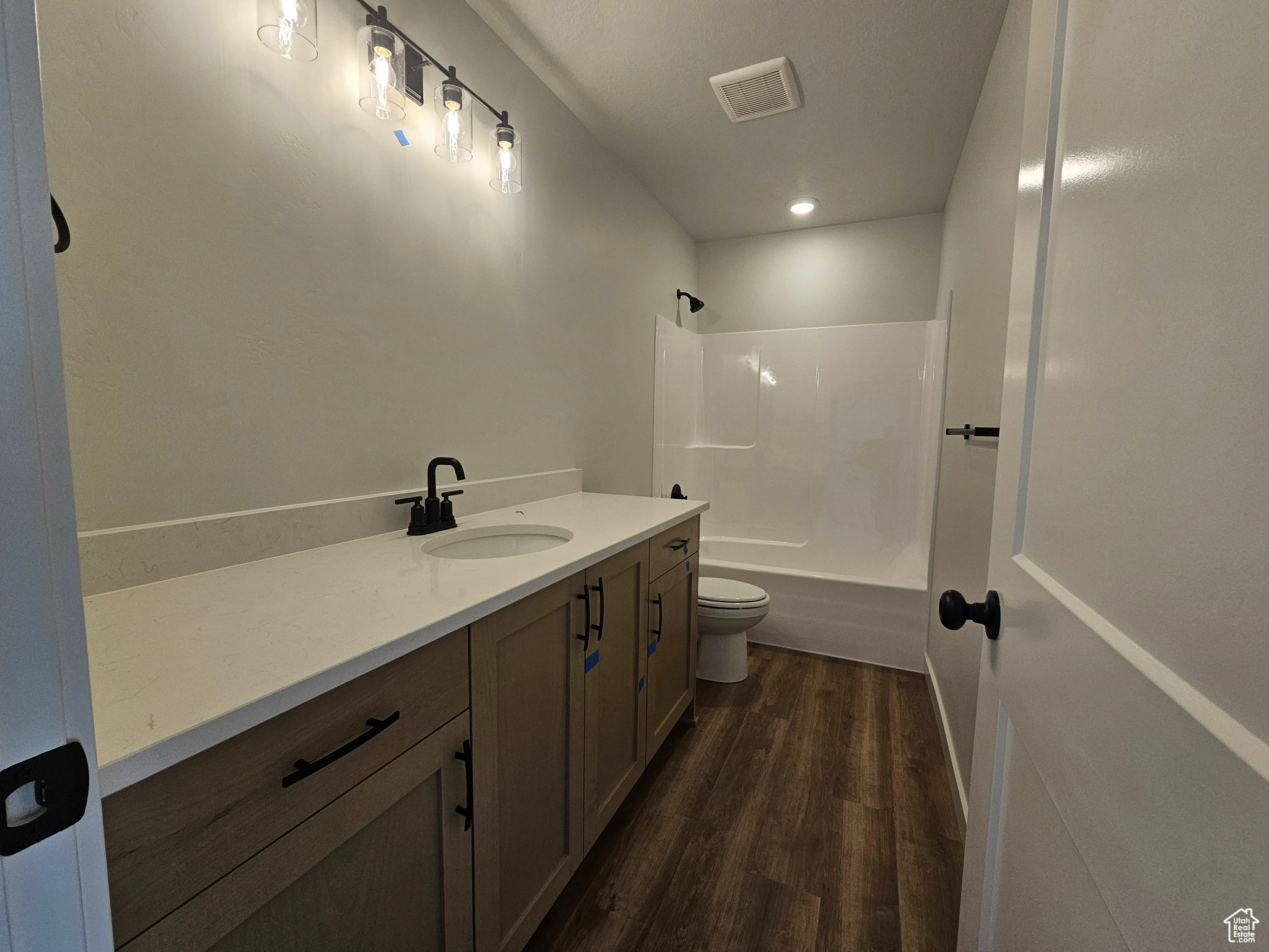 Full bathroom featuring hardwood / wood-style floors, vanity, toilet, and washtub / shower combination